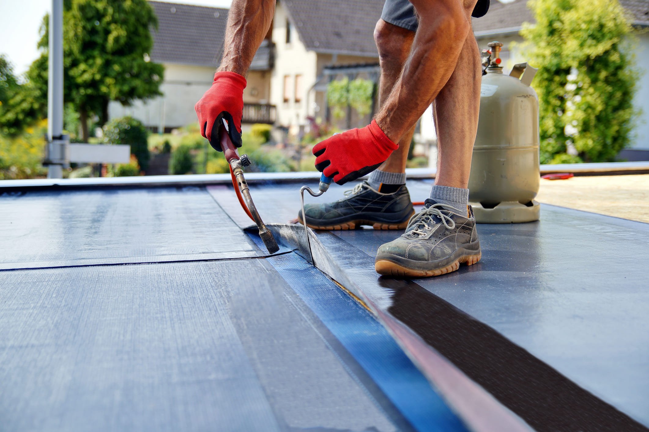 Worker repairing torch-on bitumen membrane on a flat roof using propane torch.