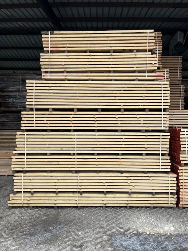 Stacked wooden planks secured with white straps at a lumberyard or hardware store.
