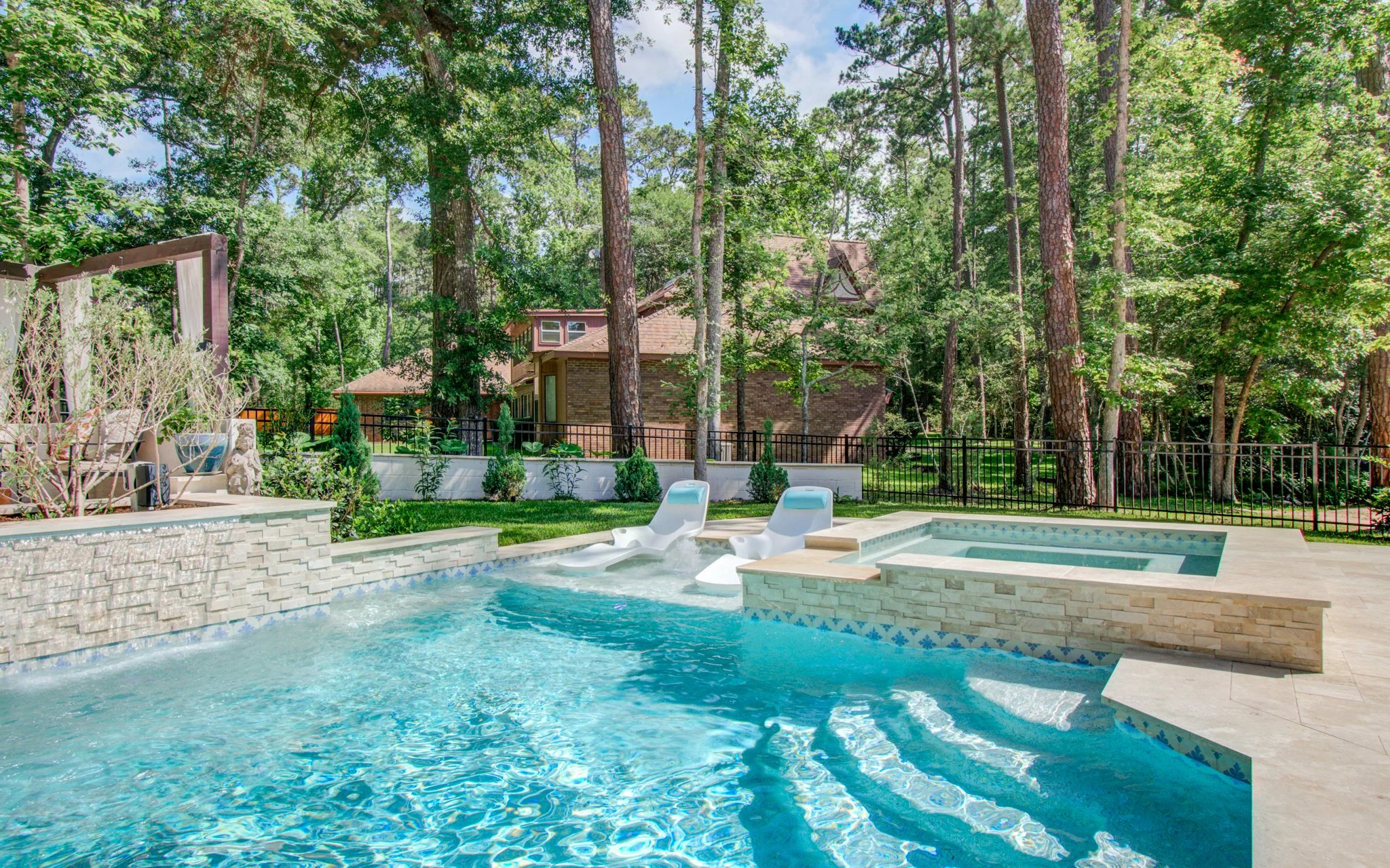 Backyard with swimming pool, pool slide, and lounge chairs, surrounded by tall trees and a brick house in the background.