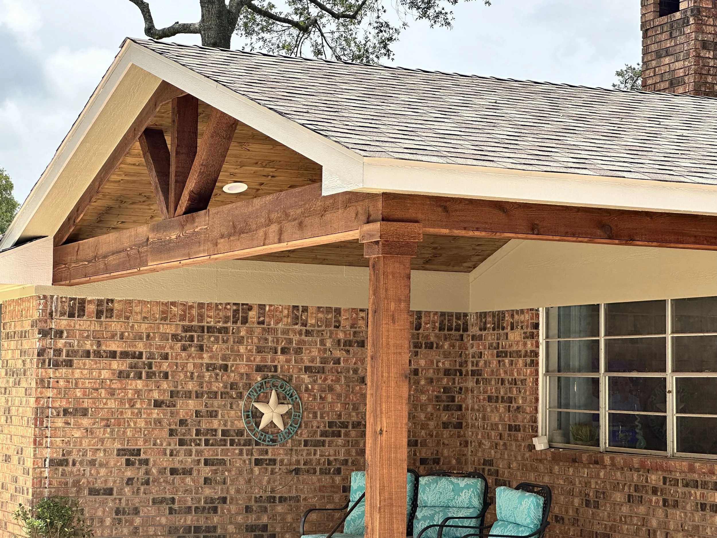 Covered patio with exposed cedar beams matching the existing brick home in Needville