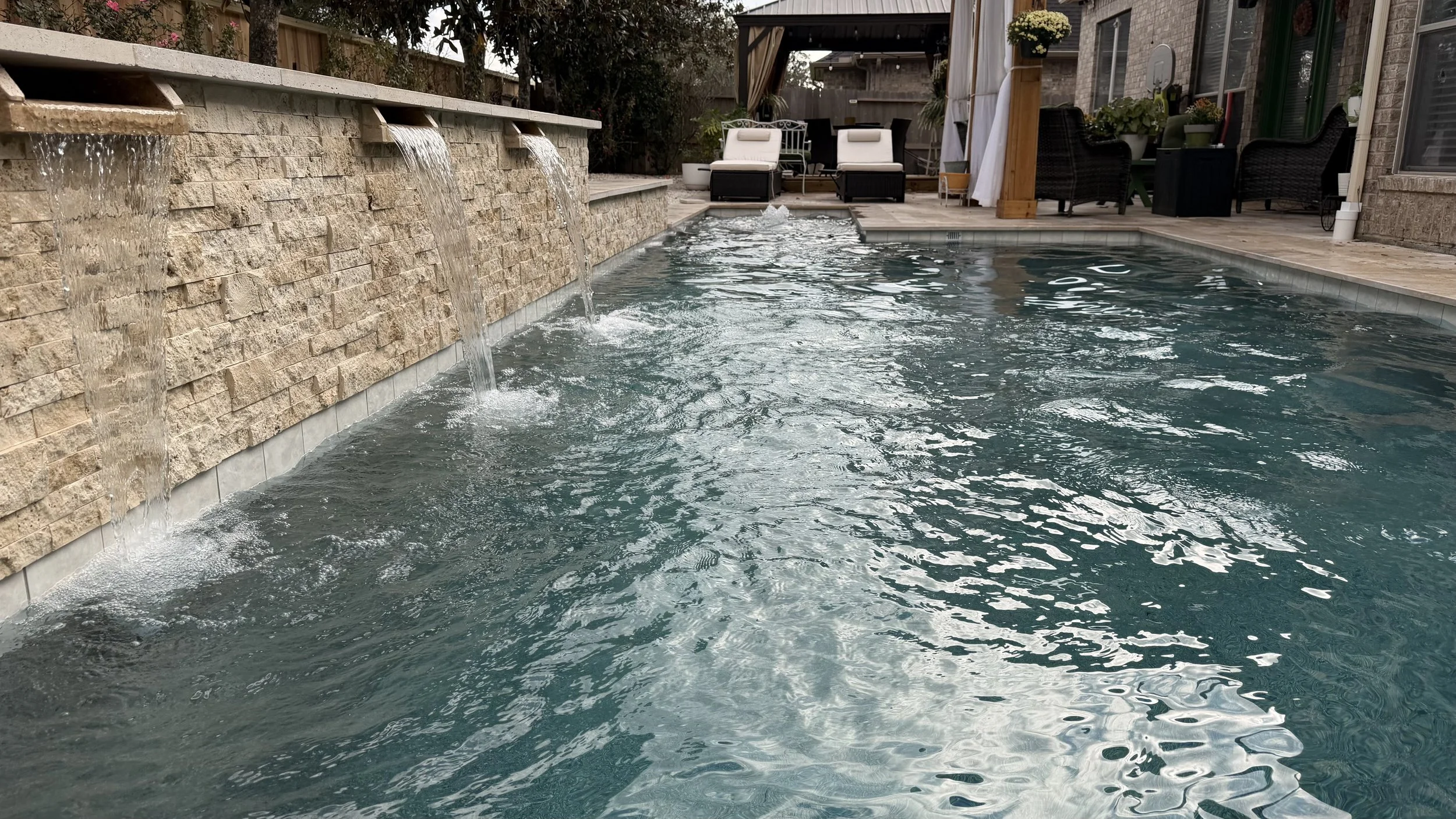 Backyard swimming pool with waterfall feature, poolside chairs, and outdoor seating area