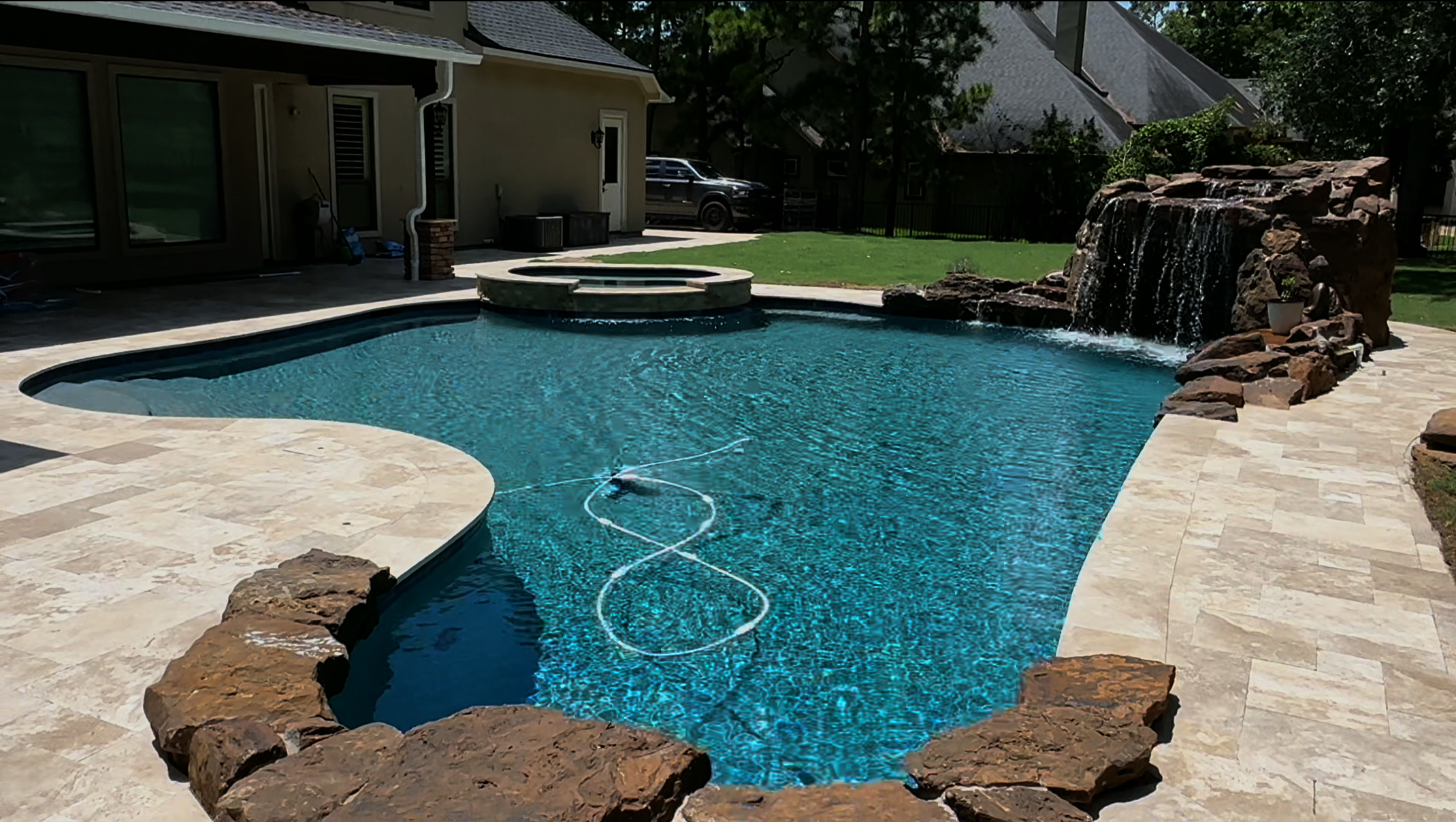 Backyard with in-ground swimming pool, waterfall feature, stone accents, grassy yard, and house in the background.
