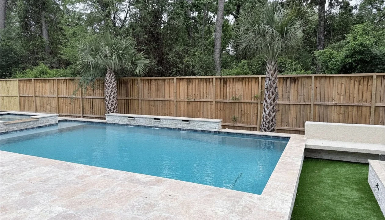 Backyard with a rectangular swimming pool, two palm trees, a wooden fence, and surrounding greenery.