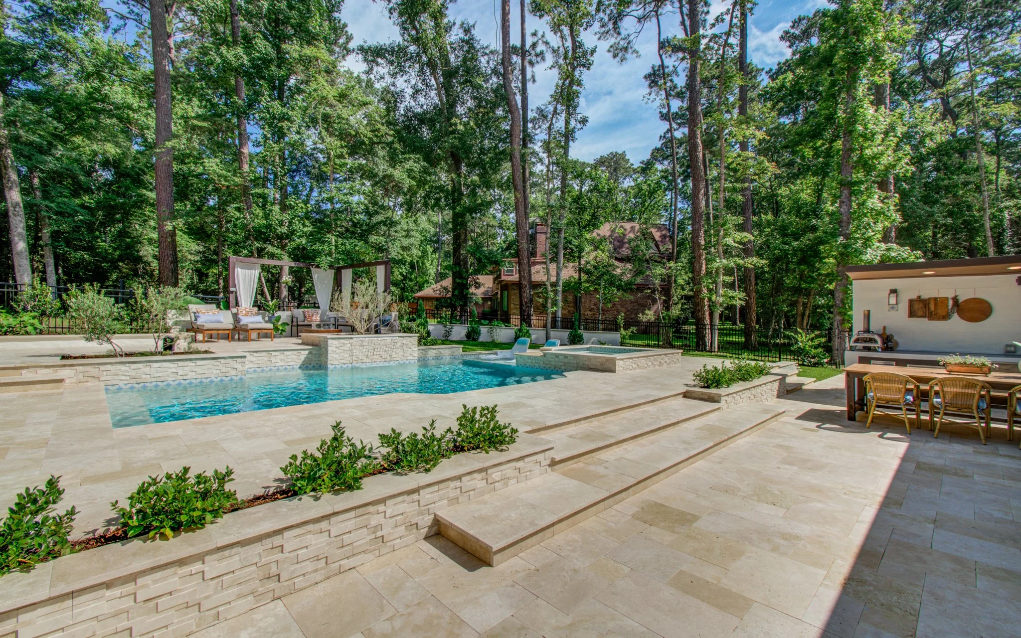 Outdoor kitchen with pizza oven and dining terrace overlooking a custom gunite pool