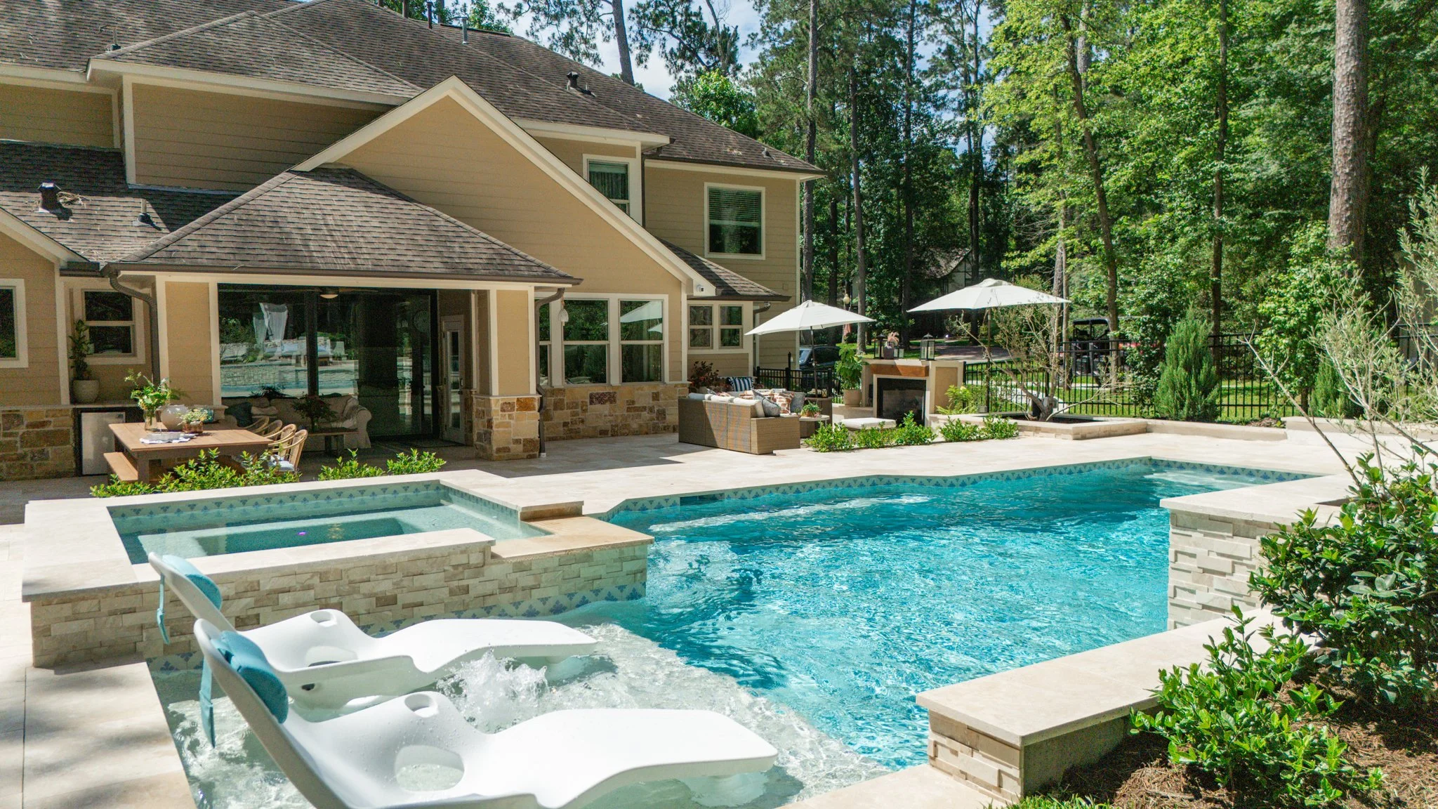 A backyard with a swimming pool, poolside seating, umbrellas, and a modern house surrounded by trees.