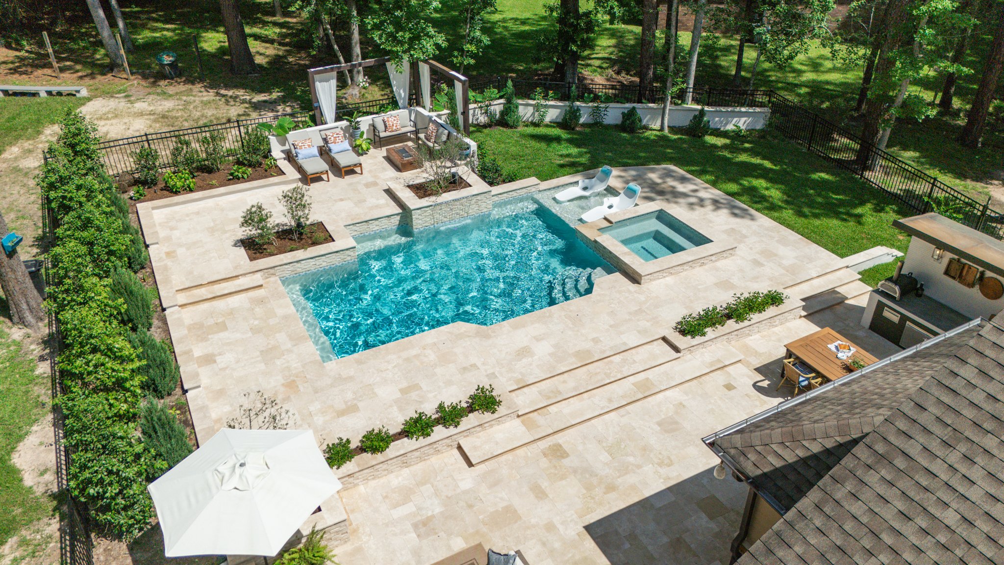 Geometric pool with sheer descent water feature and ivory travertine terraces in Conroe, TX