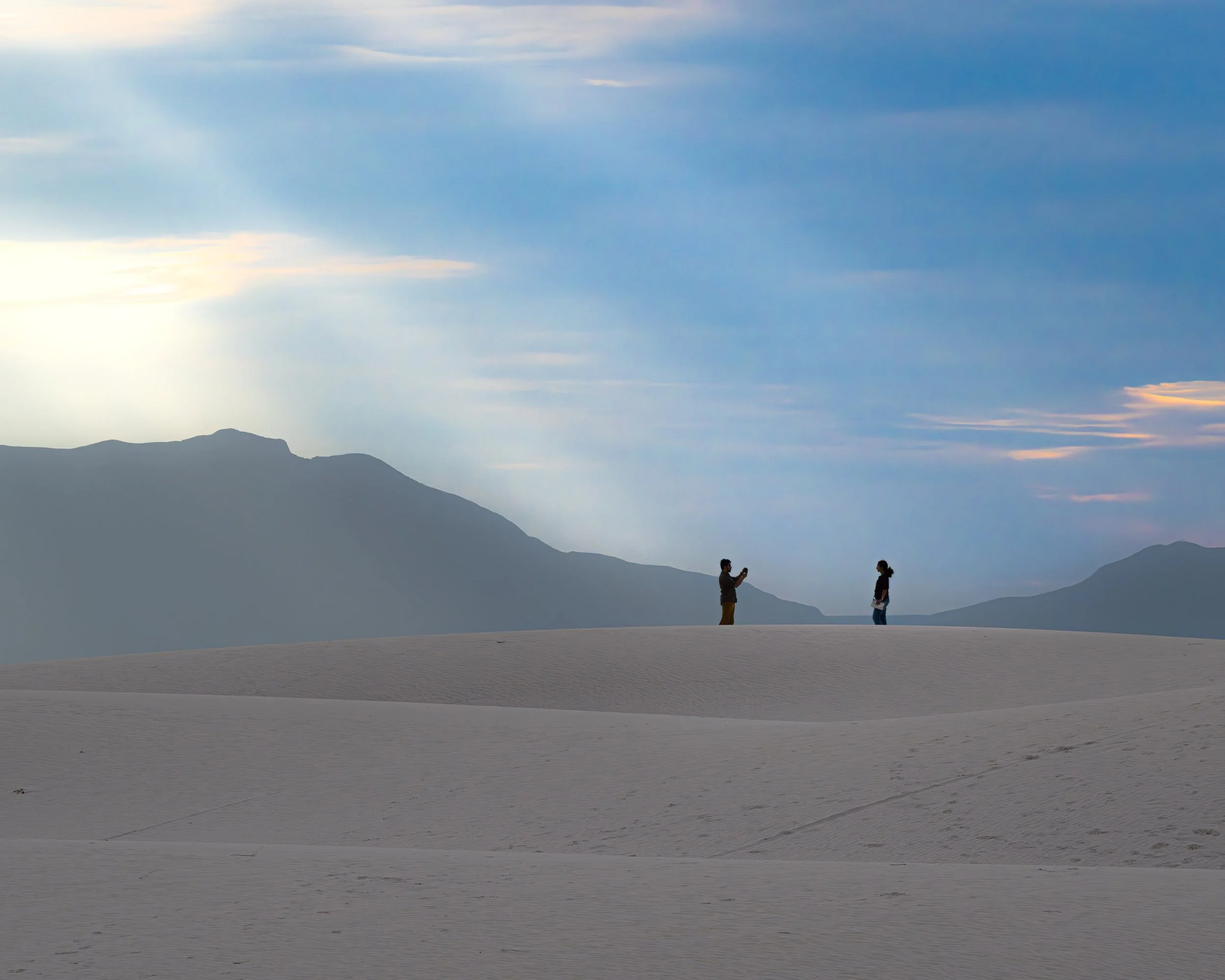 A silhouetted couple takes a photo on the dunes of White Sands National Park