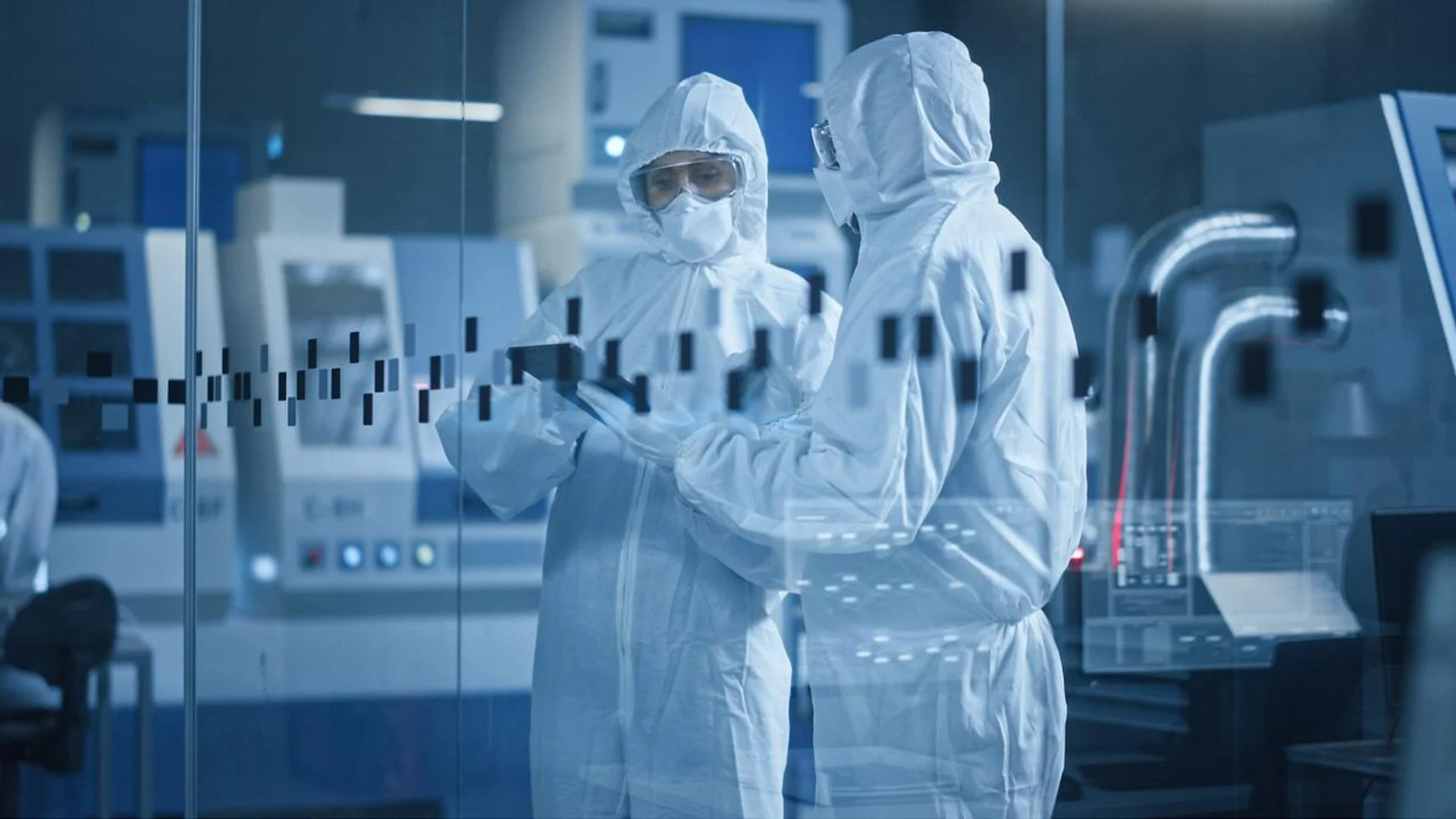 Two scientists in full protective gear reviewing data on a tablet in a high-tech laboratory.