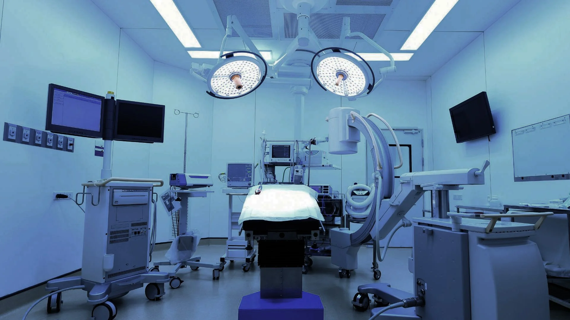 An empty hospital operating room with surgical lights, monitors, and medical equipment.
