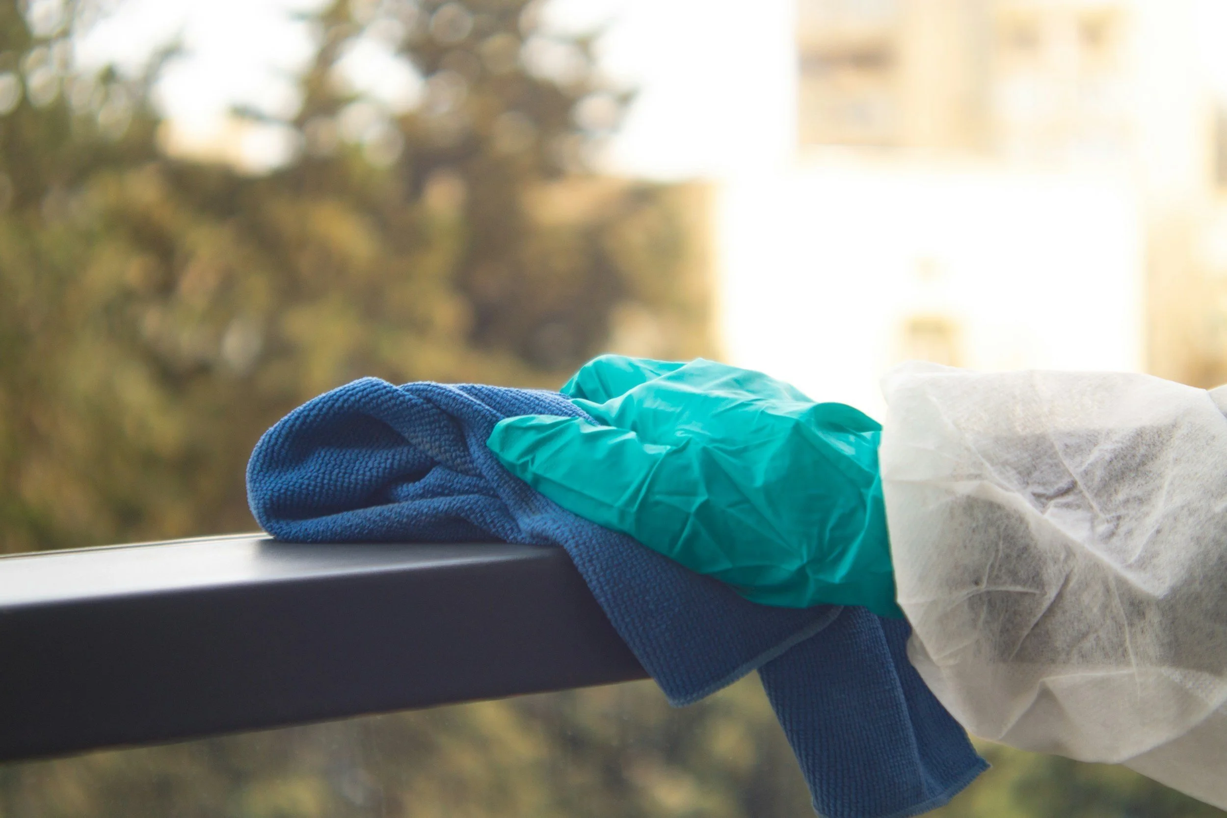 Hand wearing a green glove cleaning a glass surface with a blue cloth