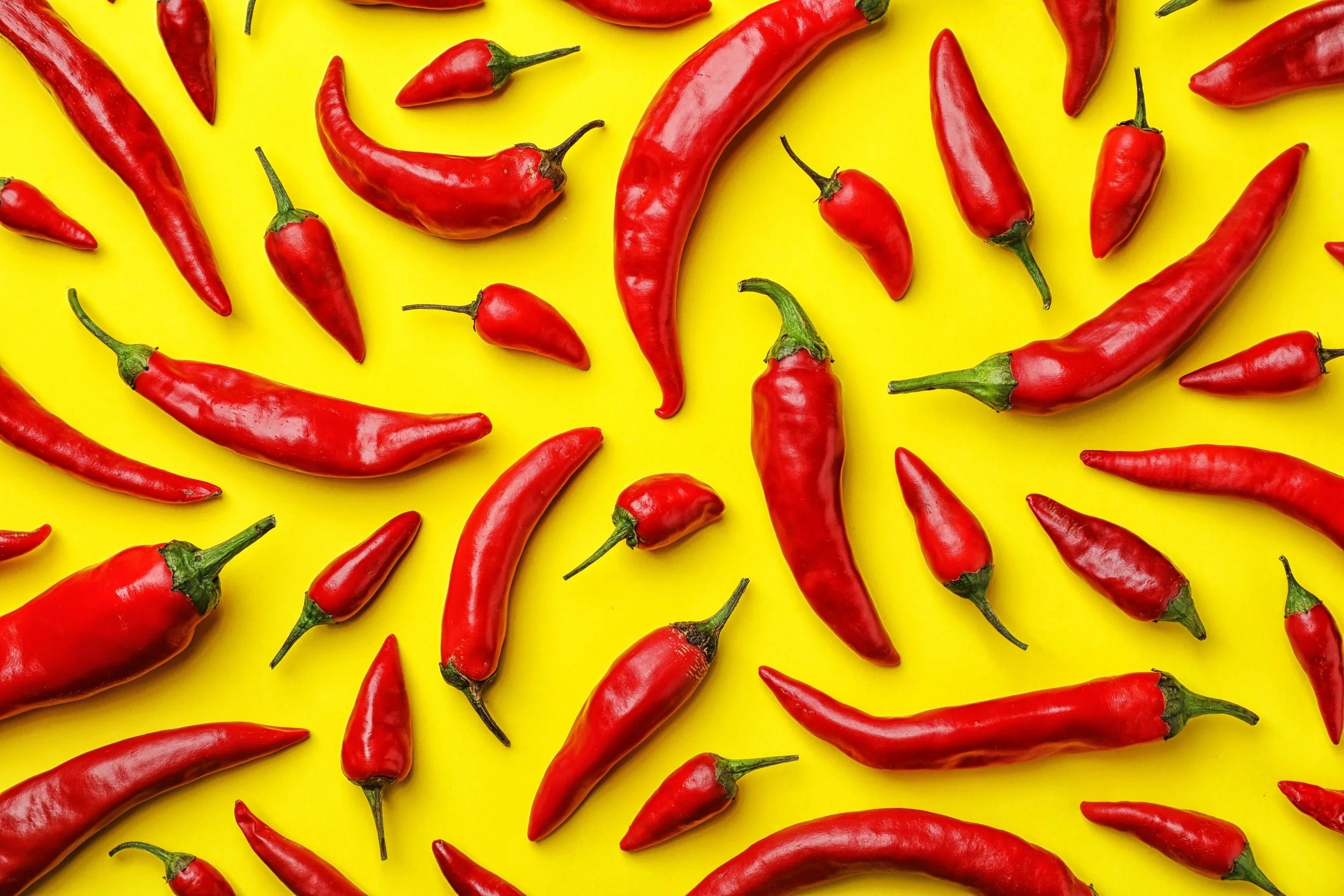 Red chili peppers scattered on a bright yellow background.