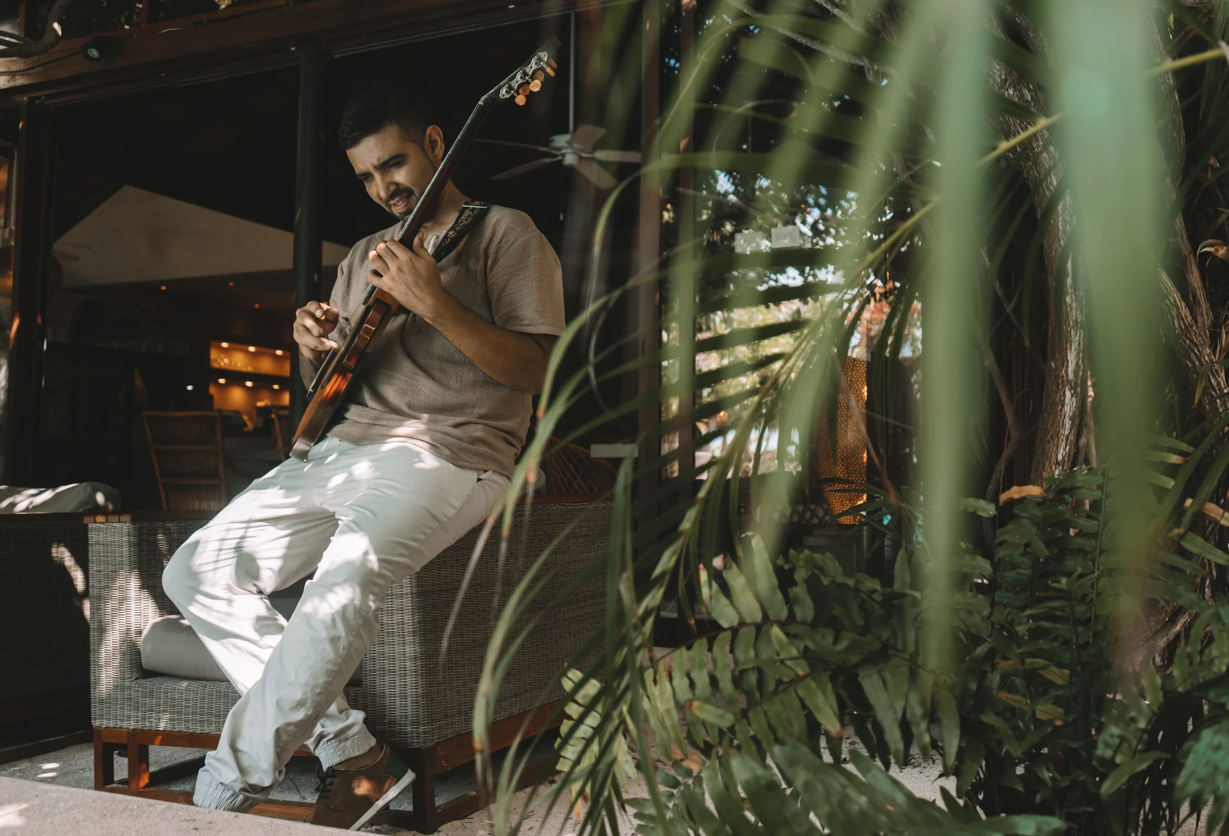 Hombre tocando guitarra eléctrica en un ambiente al aire libre rodeado de plantas.