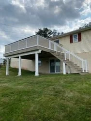 A new deck build by Schrock Exteriors featuring a dry space underneath the deck with deck privacy railing and cable railing leading down the steps. Timbertech Azek low maintenance decking, fascia, and drop beam wrap.