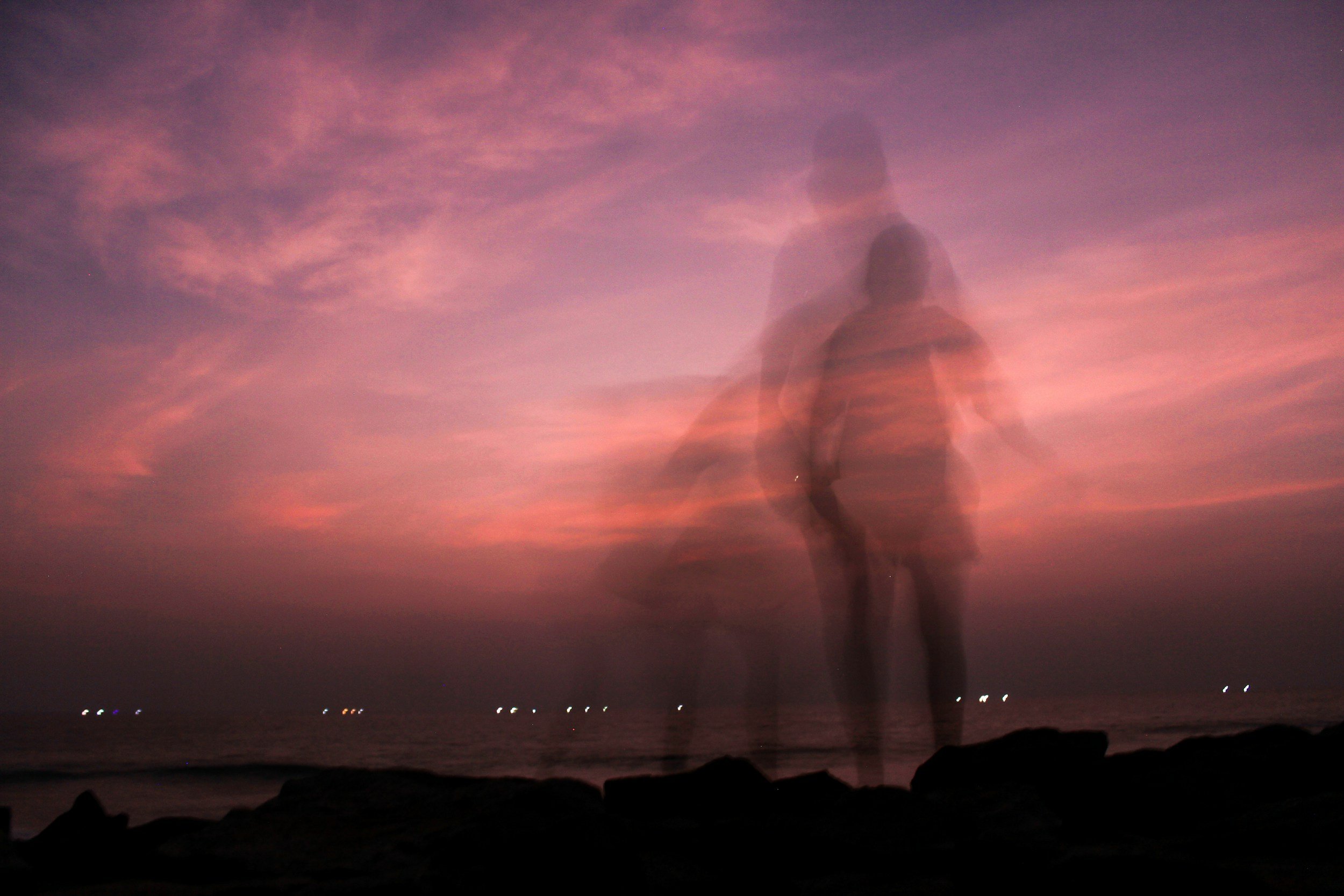 Blurred silhouette of two children walking on the beach at sunset with a colorful sky in the background.