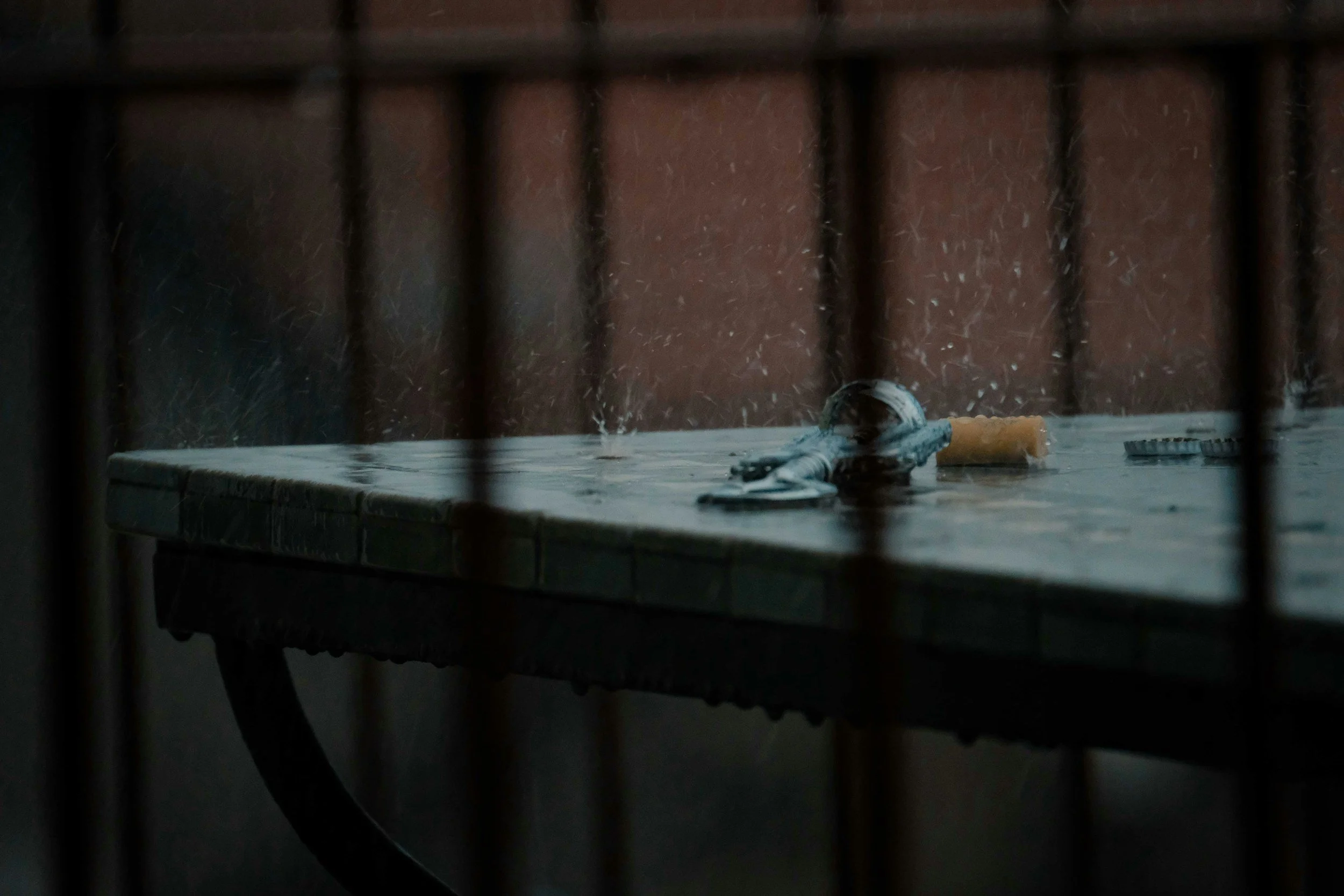 An empty table viewed through a fence, with objects including keys, a roll of tape, and a small round dish on the table.