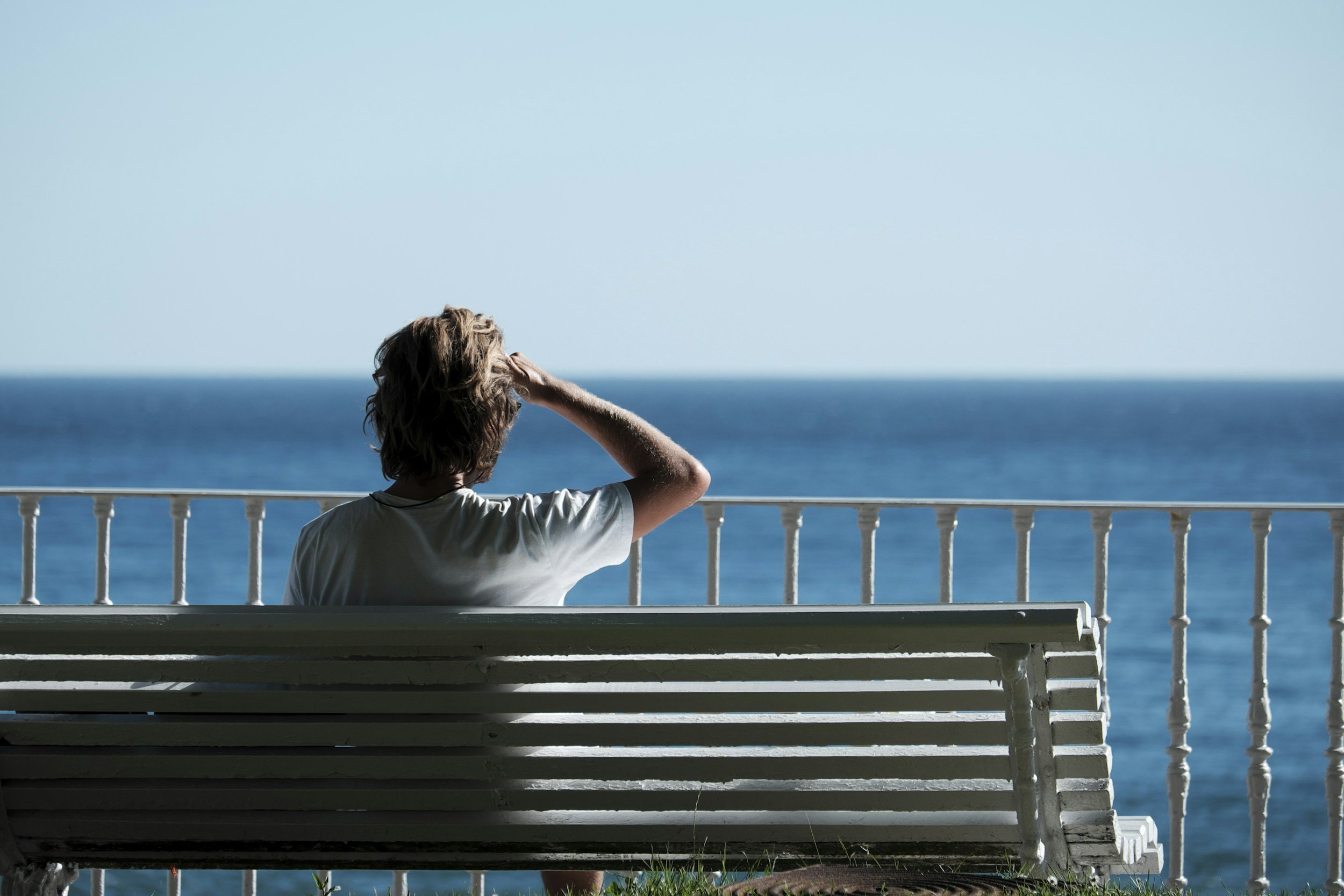 Person sitting on a white bench with a view of the ocean in the background, saluting the horizon.