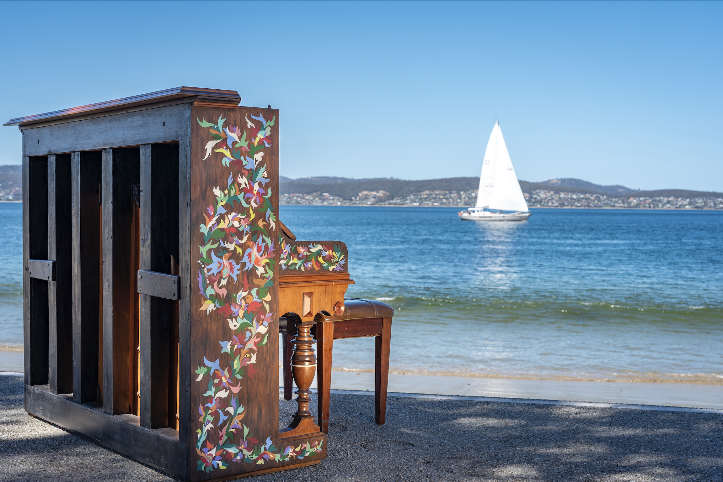 Hand-painted cultural mural on the Piano of Tasmania placed on a Tasmanian beach, featuring symbolic bird motifs