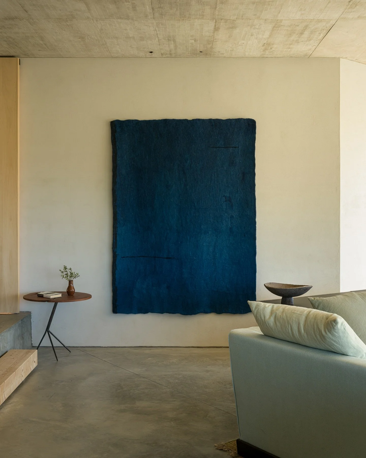 A deep, textural felt work by @morevi.studio anchors the space at @canaserra_melides, its indigo surface quietly absorbing and reflecting light throughout the day. Beside it, a ceramic by @marlieshuybs.be rests with quiet poise&mdash;two pieces in di