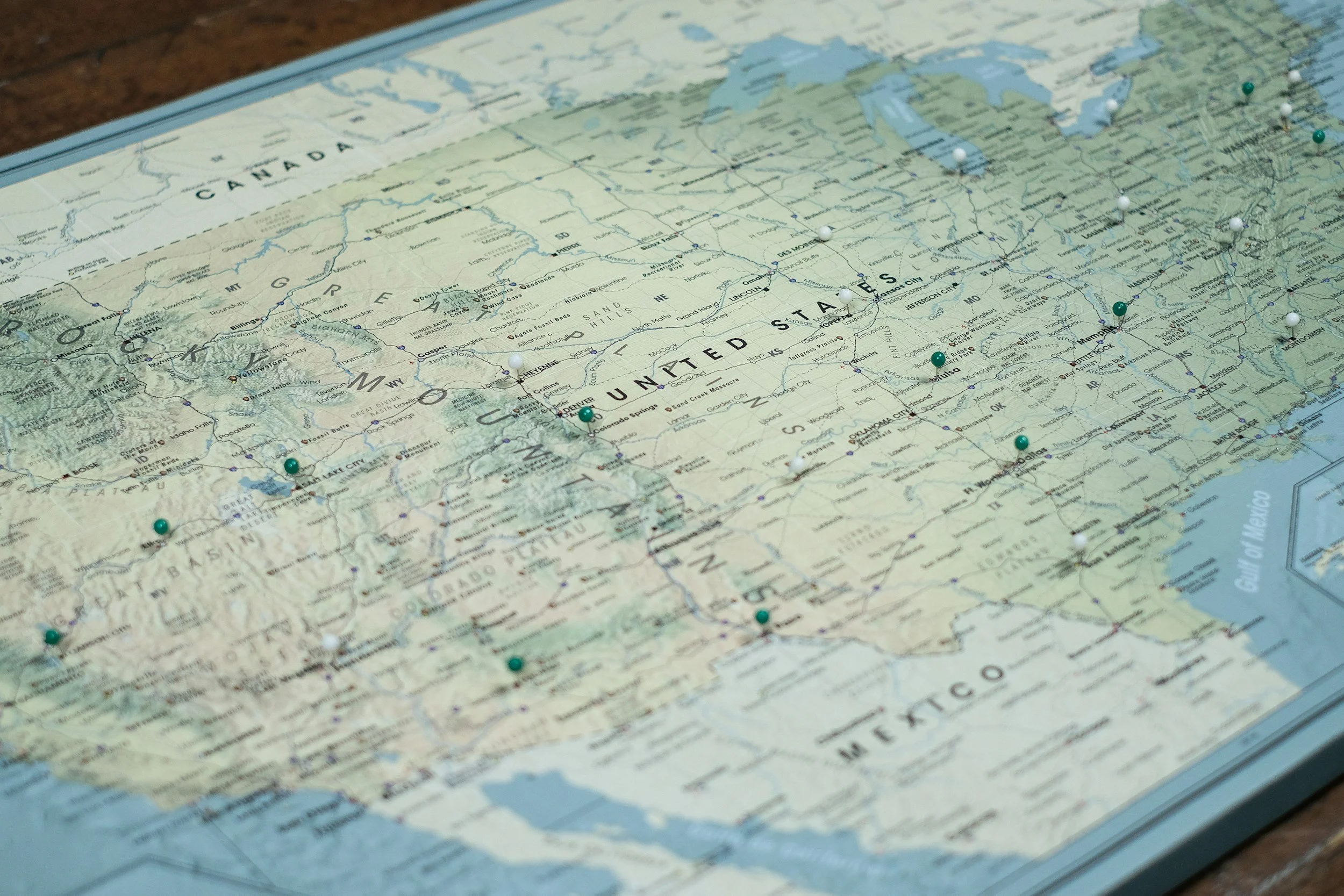 A printed map of the United States with pushpins marking various locations across the country.