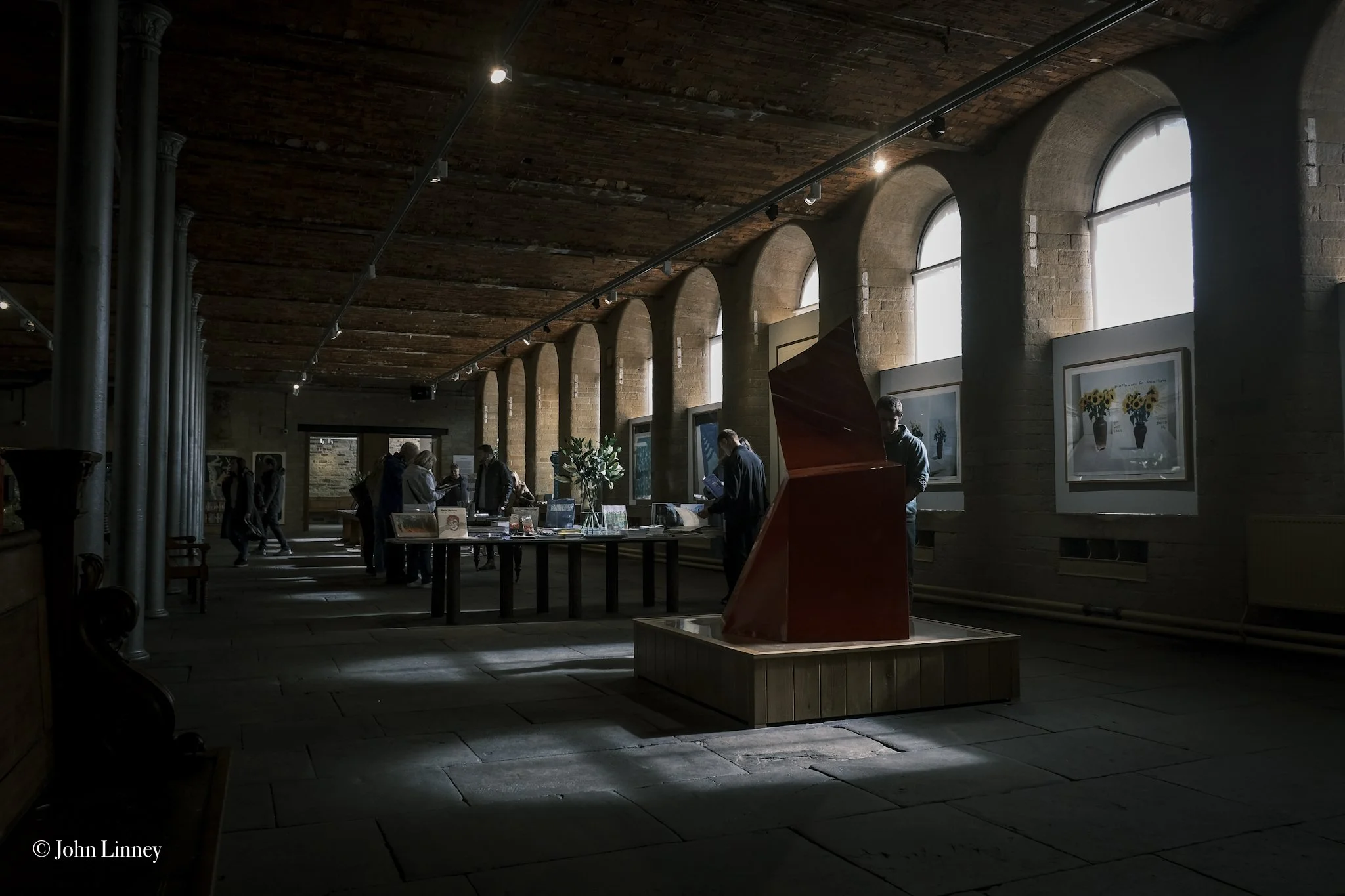 Interior of an art gallery with arched windows, artwork displays, and visitors browsing exhibits.