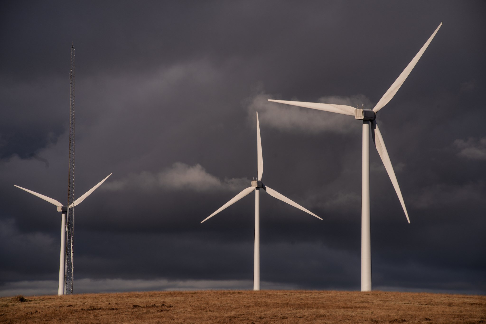 Wind turbines on a grassy hill against a dark, cloudy sky.