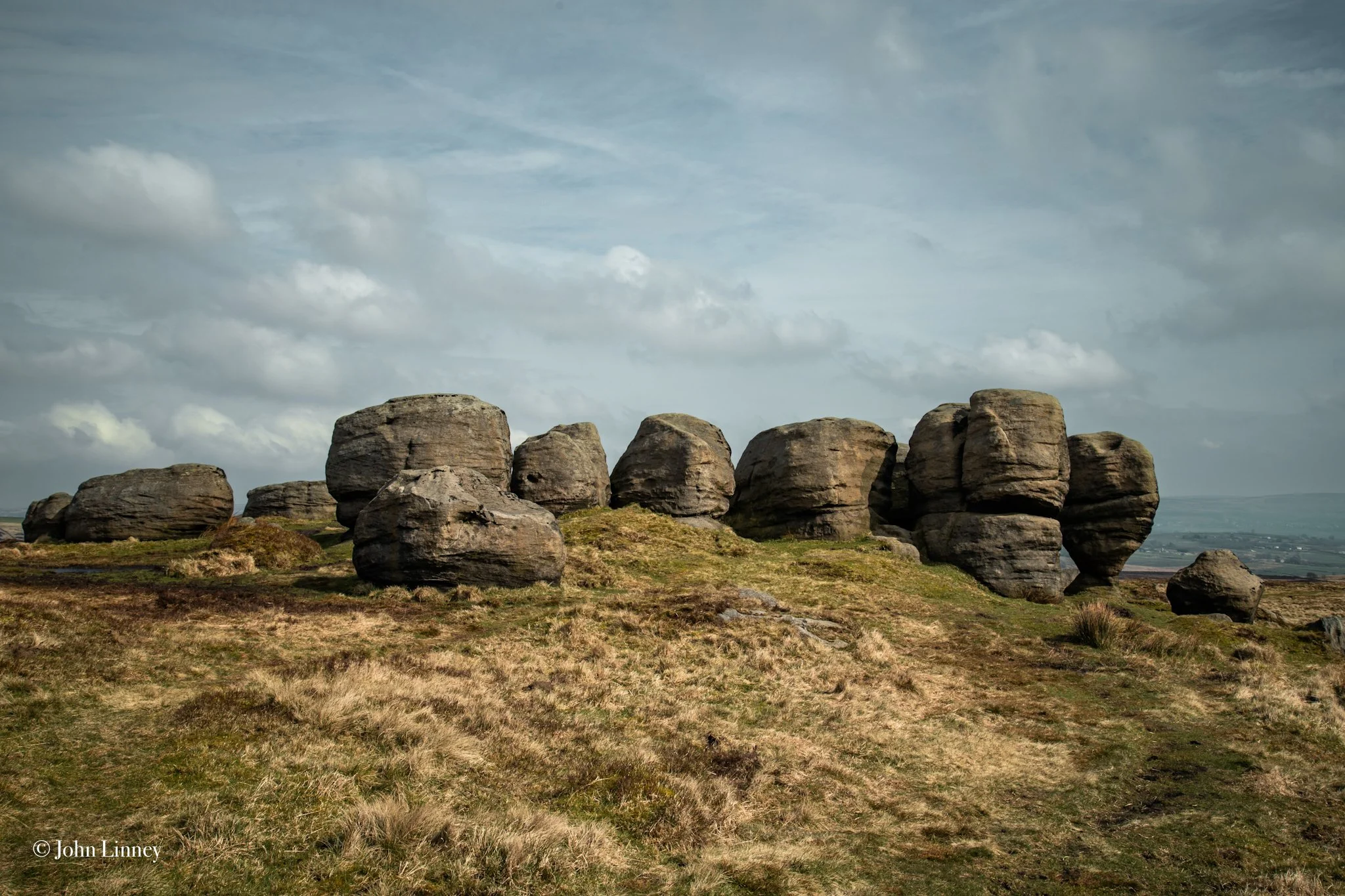 Rock formations on a grassy landscape under a cloudy sky.