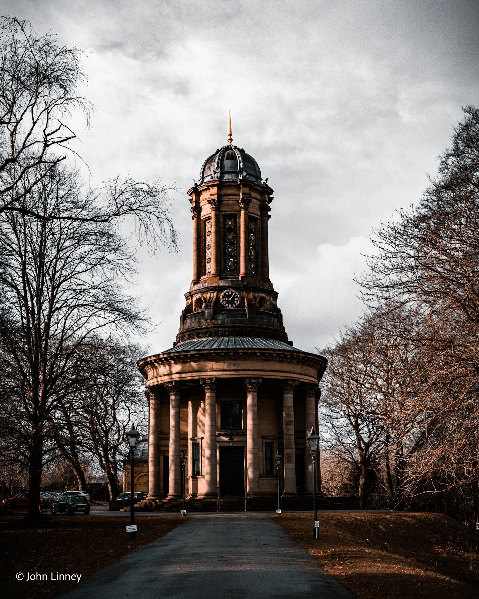 A neo-classical building with columns and a clock tower, surrounded by trees in a park.