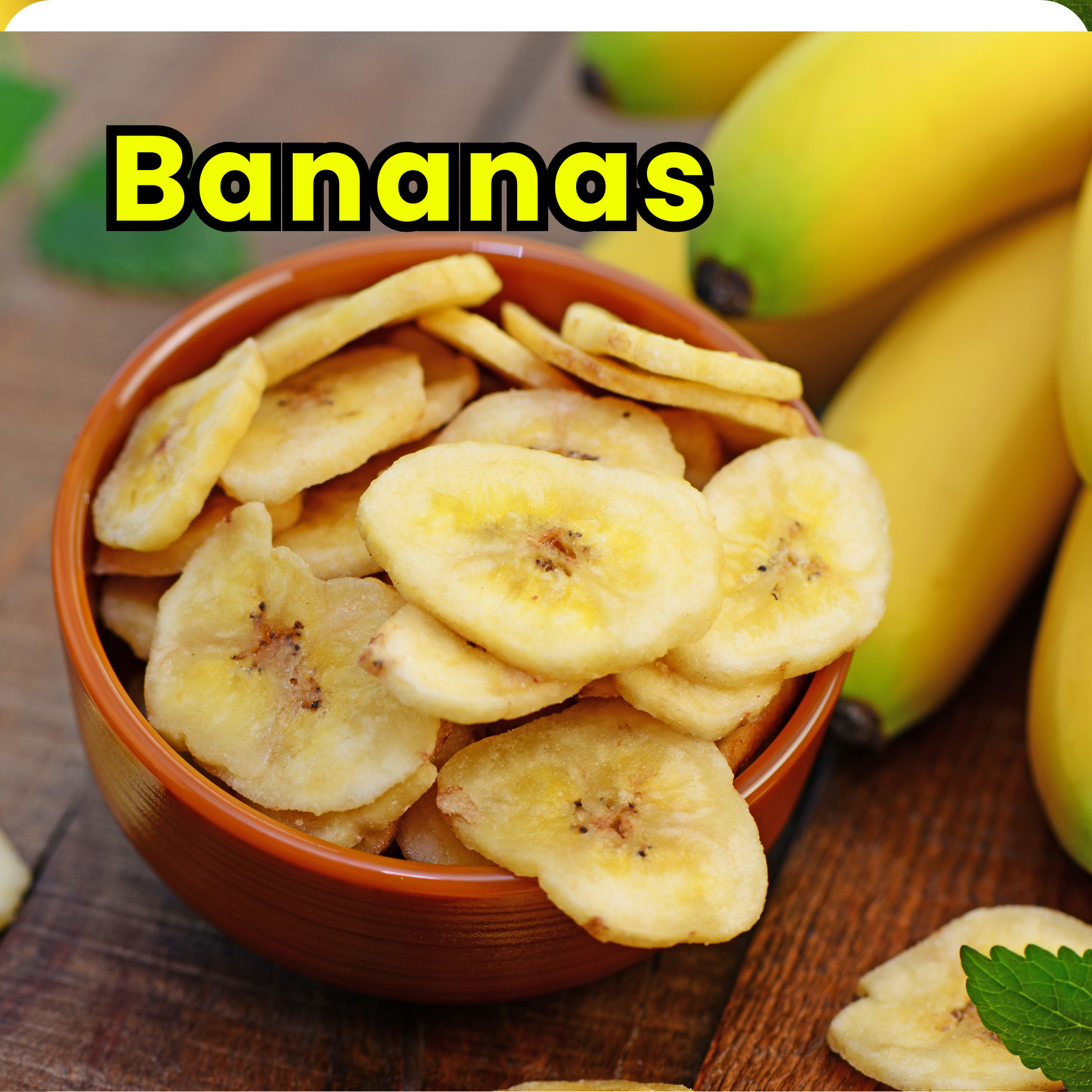 A bowl of sliced dried bananas with whole bananas in the background on a wooden surface.