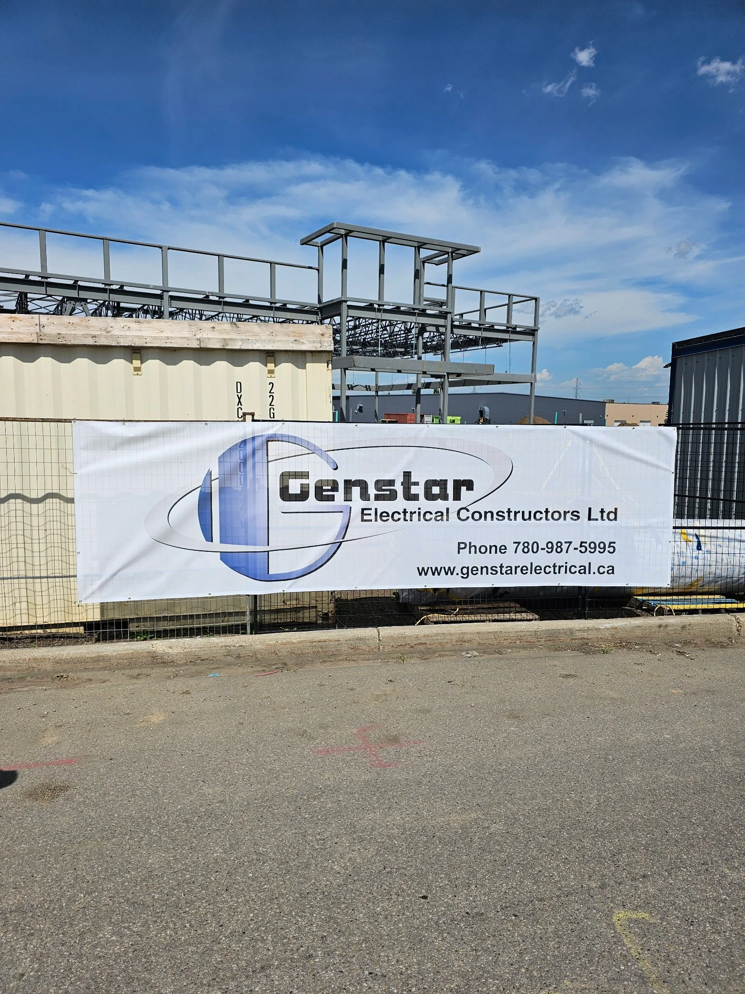 Construction site with a sign for Genstar Electrical Constructors Ltd, showing their phone number and website, with building frameworks in background under a partly cloudy sky.