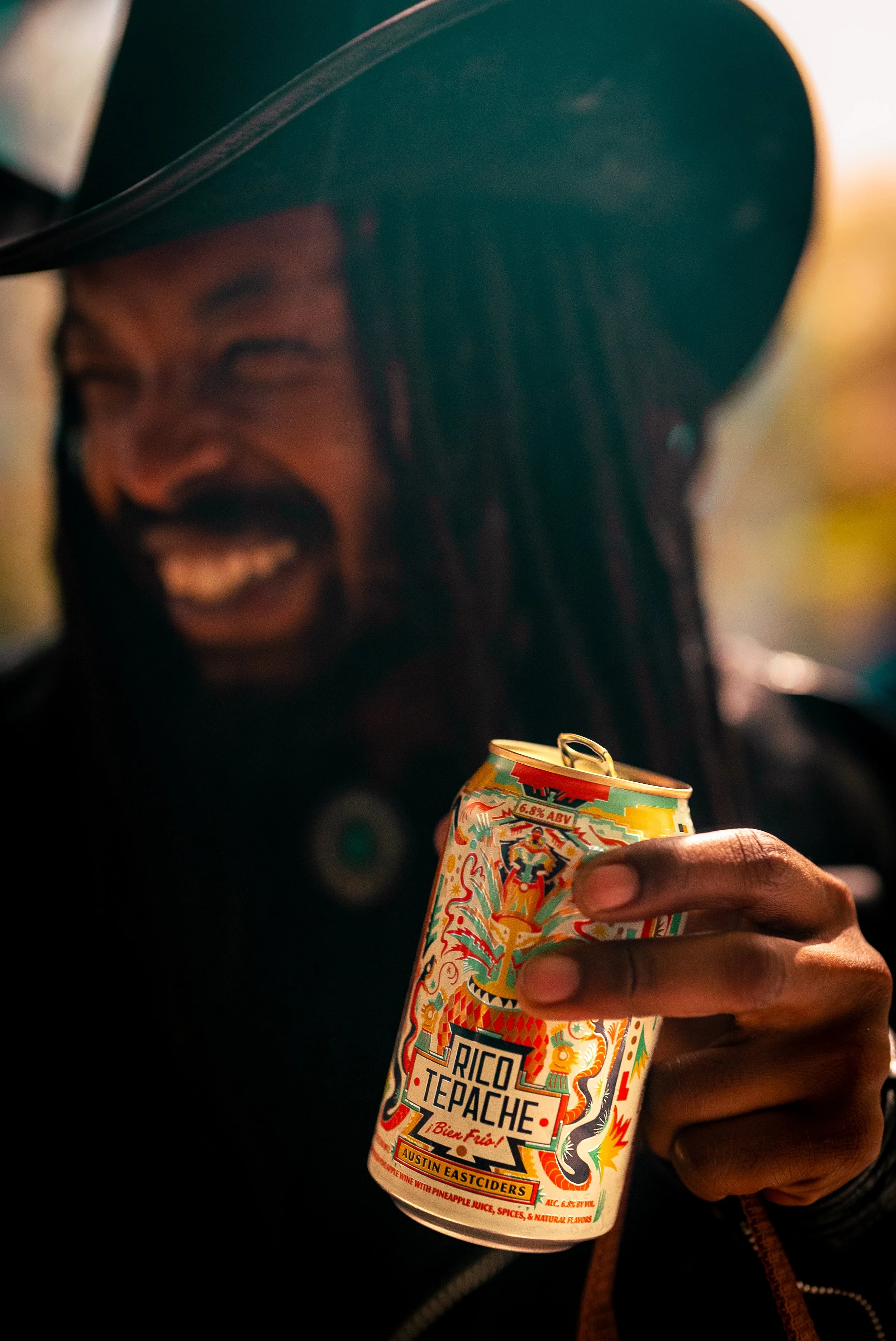 Commercial lifestyle beverage and food product photography of a stylish man in his 30s with dreadlocks holding a Rico Tepache craft beverage, using vibrant color and natural styling to create an eye-catching, high-impact image for alcohol brands, soc