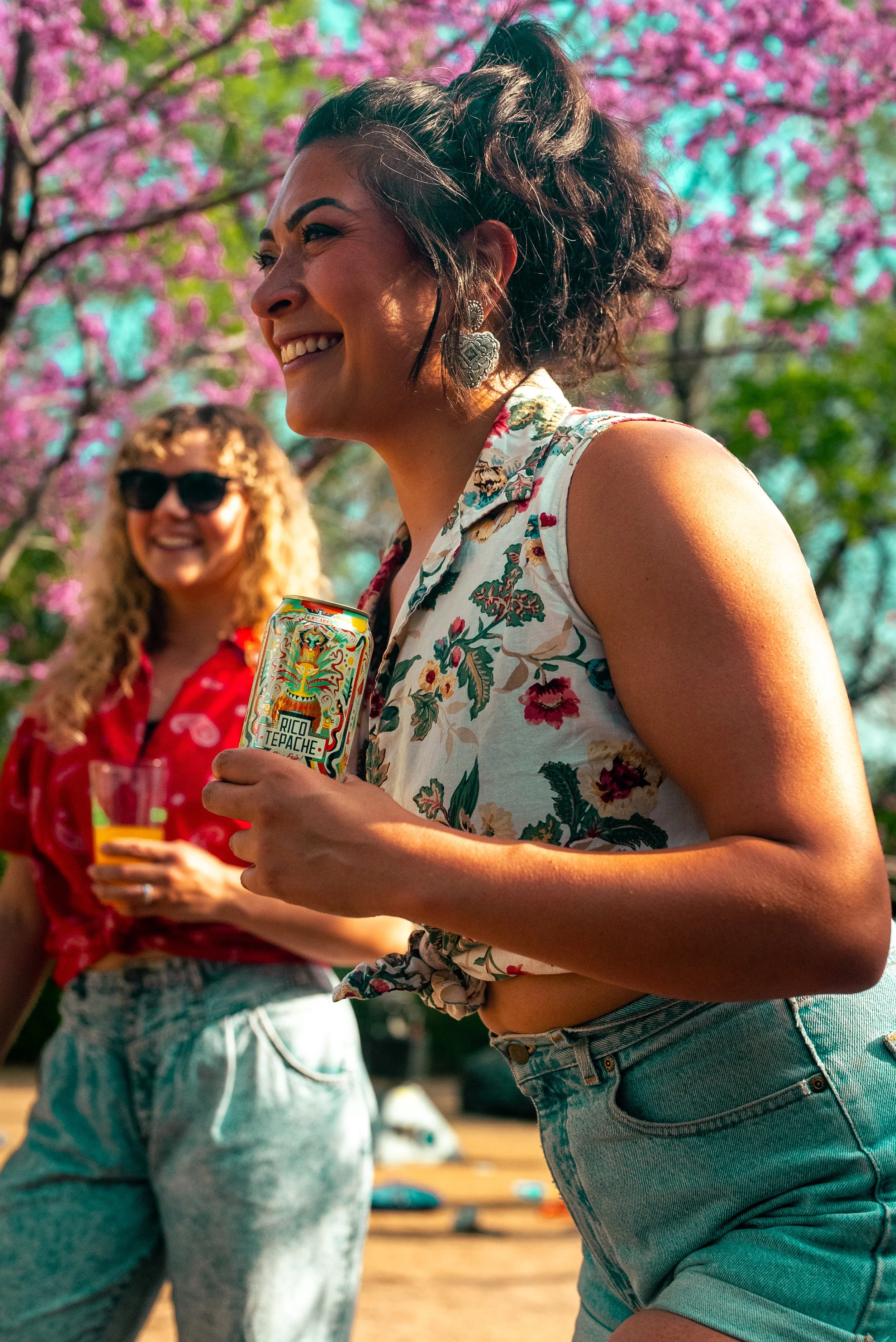 Commercial lifestyle beverage and food product photography of two stylish millennial women enjoying drinks outdoors in spring, featuring vibrant color, natural light, and blooming cherry blossoms, creating an eye-catching, high-impact image.