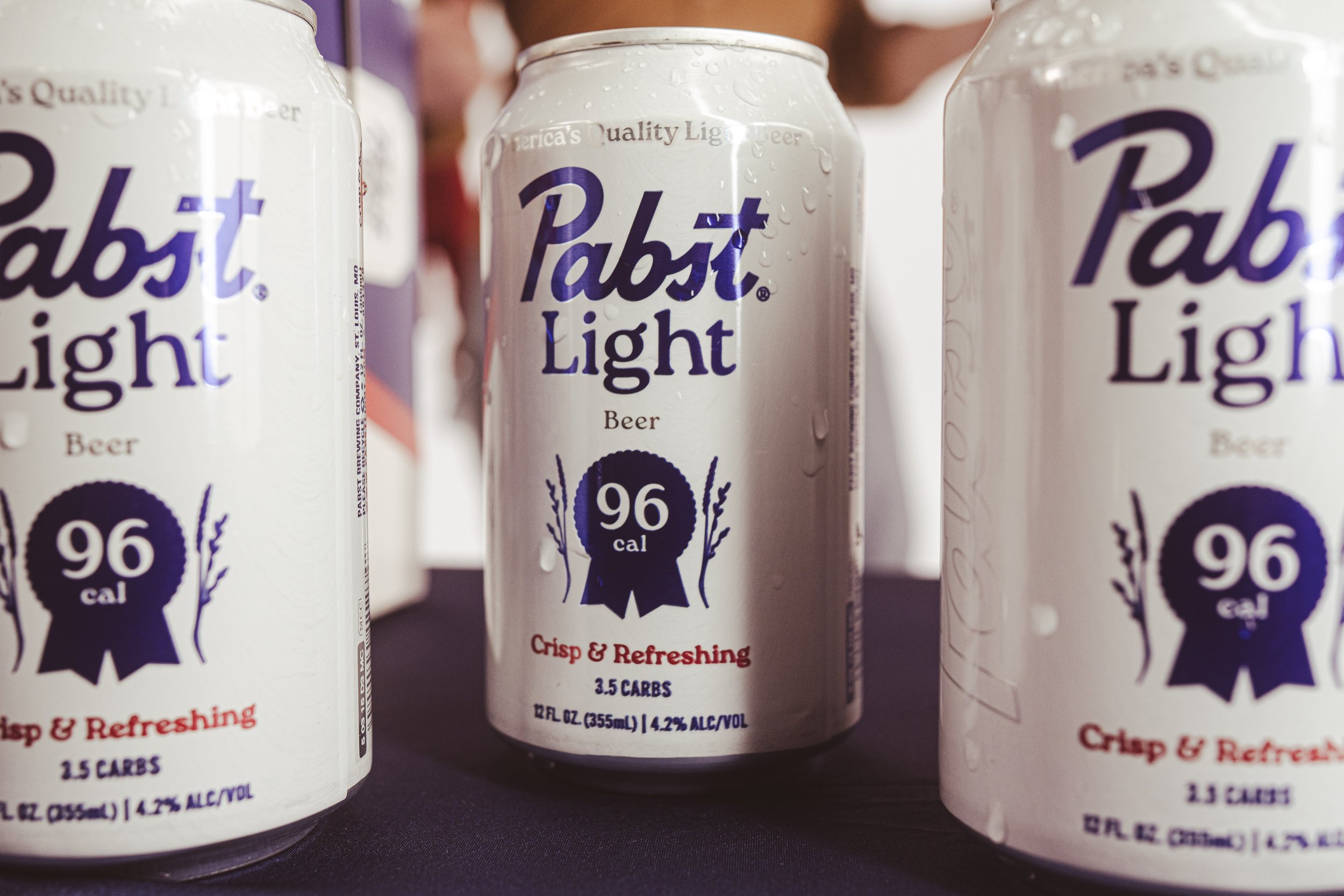 Commercial beverage and food product photography close-up of three Pabst Light beer cans with condensation on a black surface, using dramatic lighting and contrast to create an eye-catching, high-impact visual for social media and advertising content