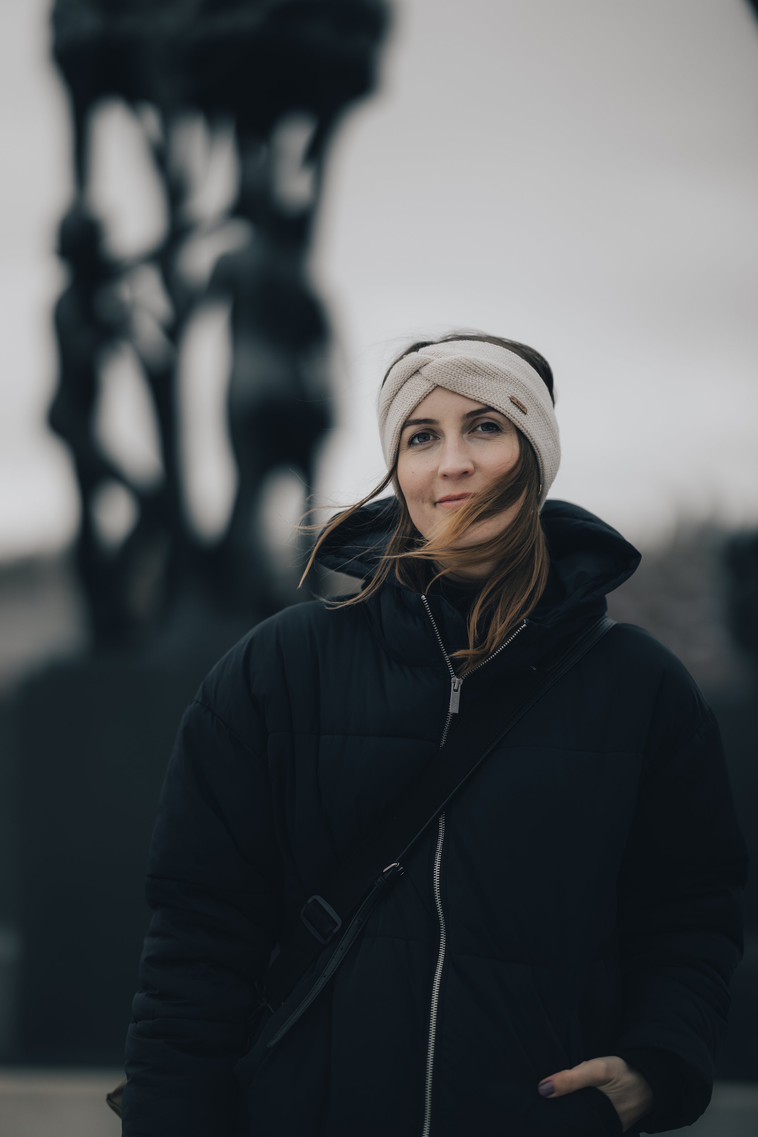 Kvinne i svart jakke og hvitt panneband foran skulptur.
