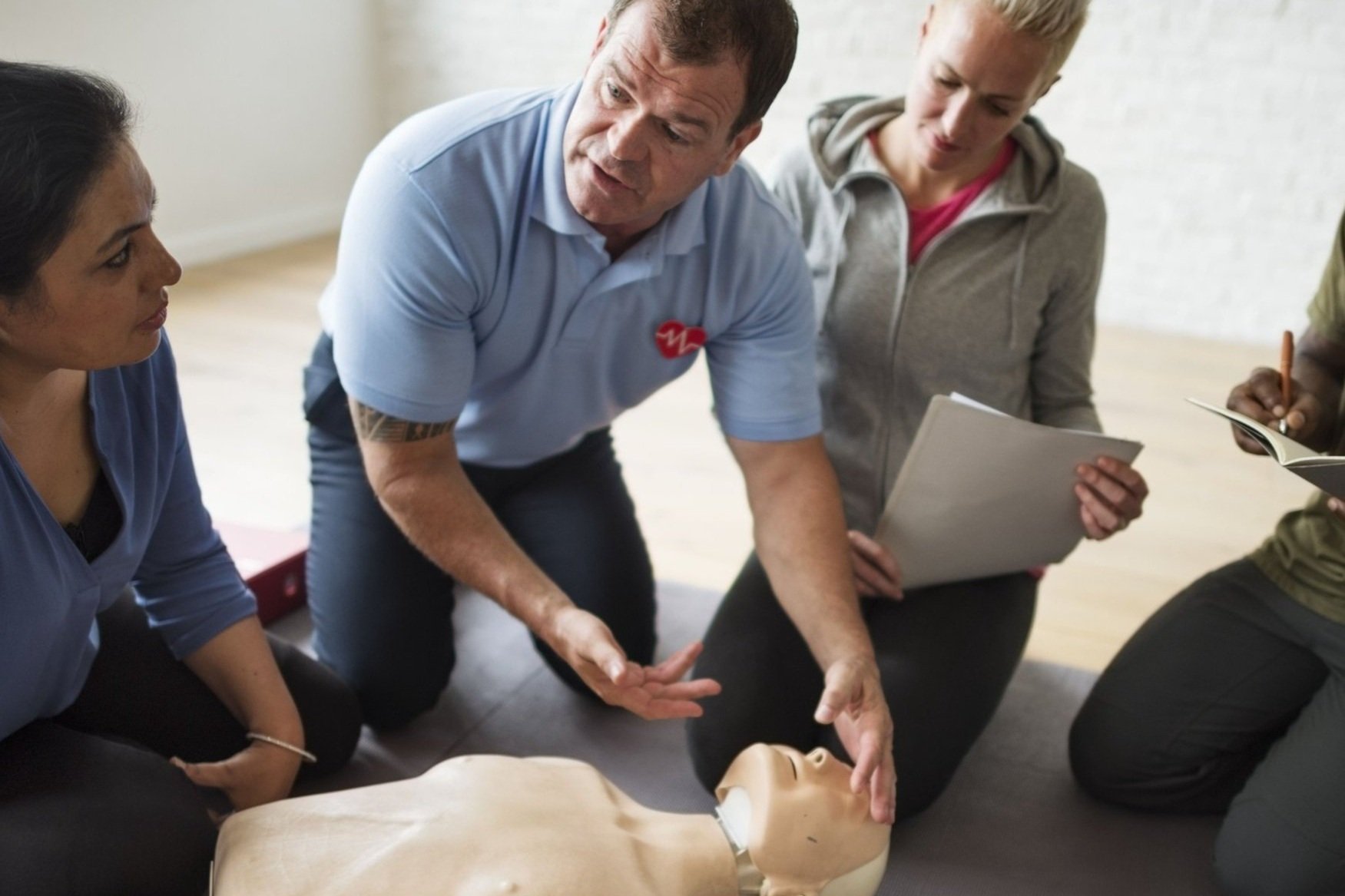A group of people participating in a CPR training session, practicing on a medical mannequin lying on the floor.