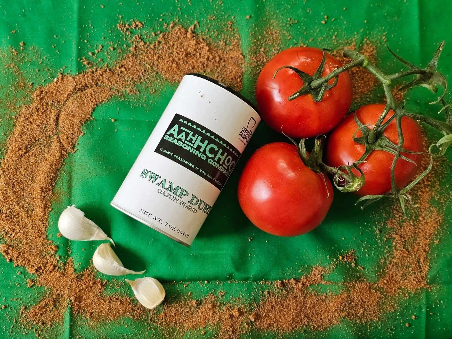 Aahh Choo Swamp Dust Cajun Blend with tomatoes, garlic, and seasoning on a green background.