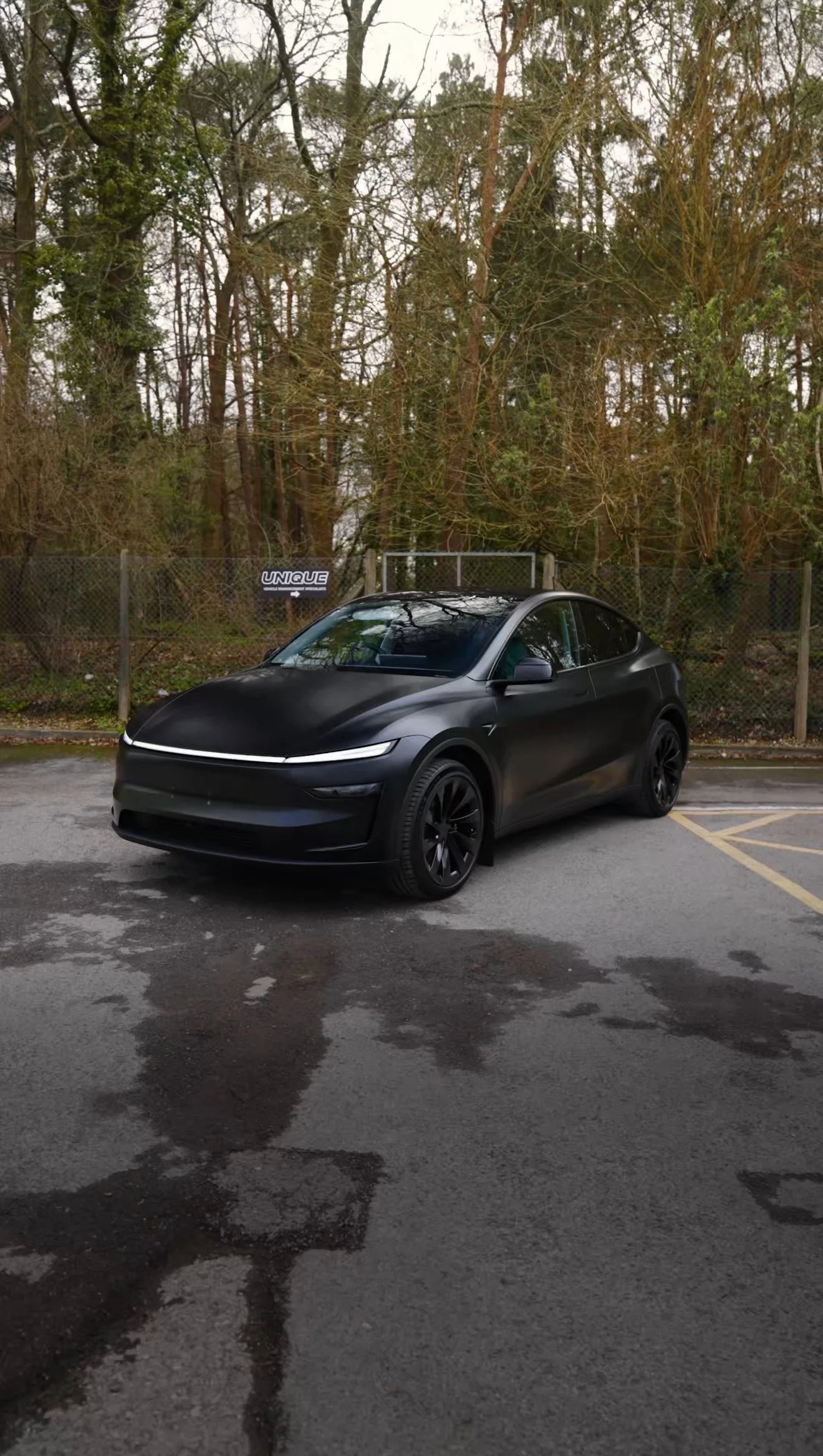 A black electric SUV parked in an outdoor parking lot with trees and a chain-link fence in the background.