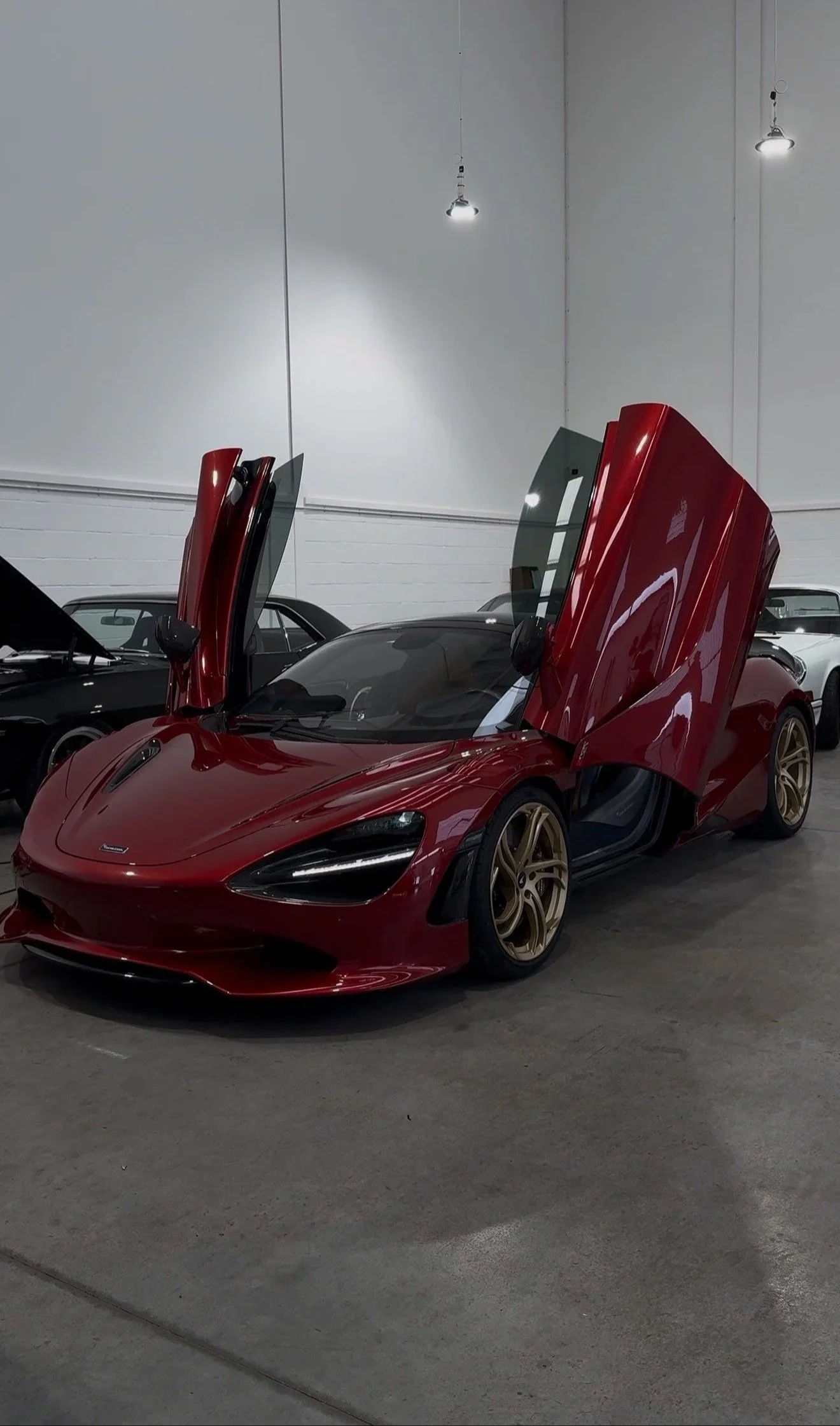A red sports car with its gullwing doors open, parked inside a showroom with other cars and white walls.