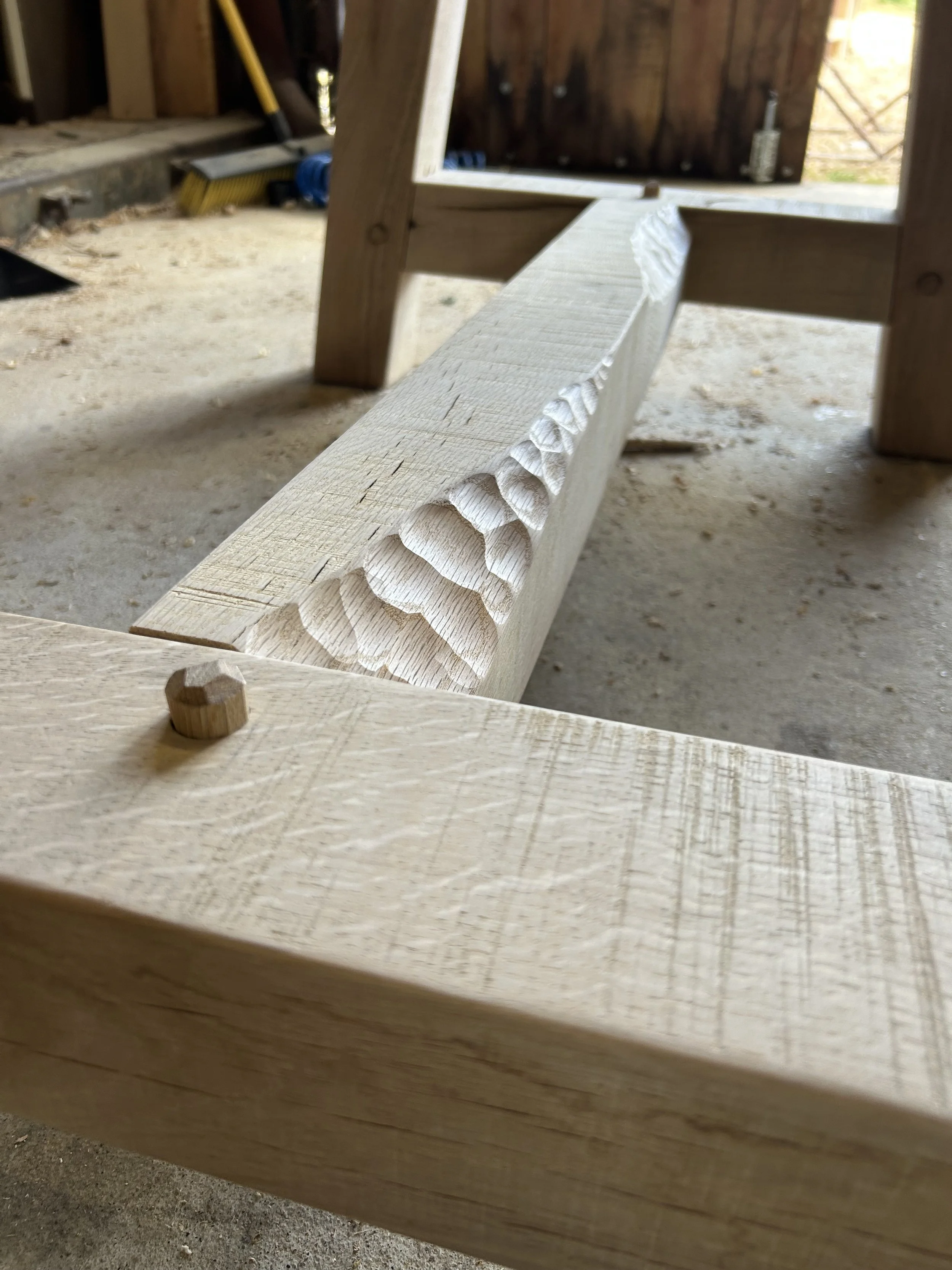Close-up of a partially carved wooden piece on a workbench, showing scalloped grooves.