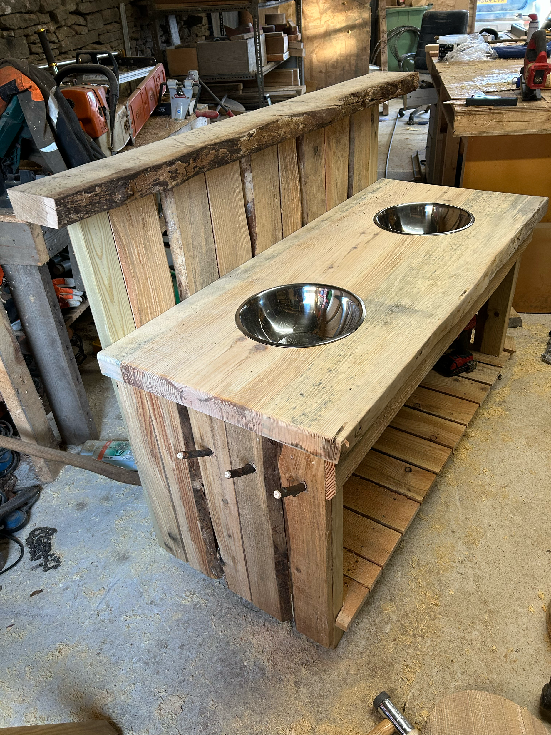 A rustic wooden vanity with two stainless steel sinks, made from reclaimed wood in a woodworking shop.
