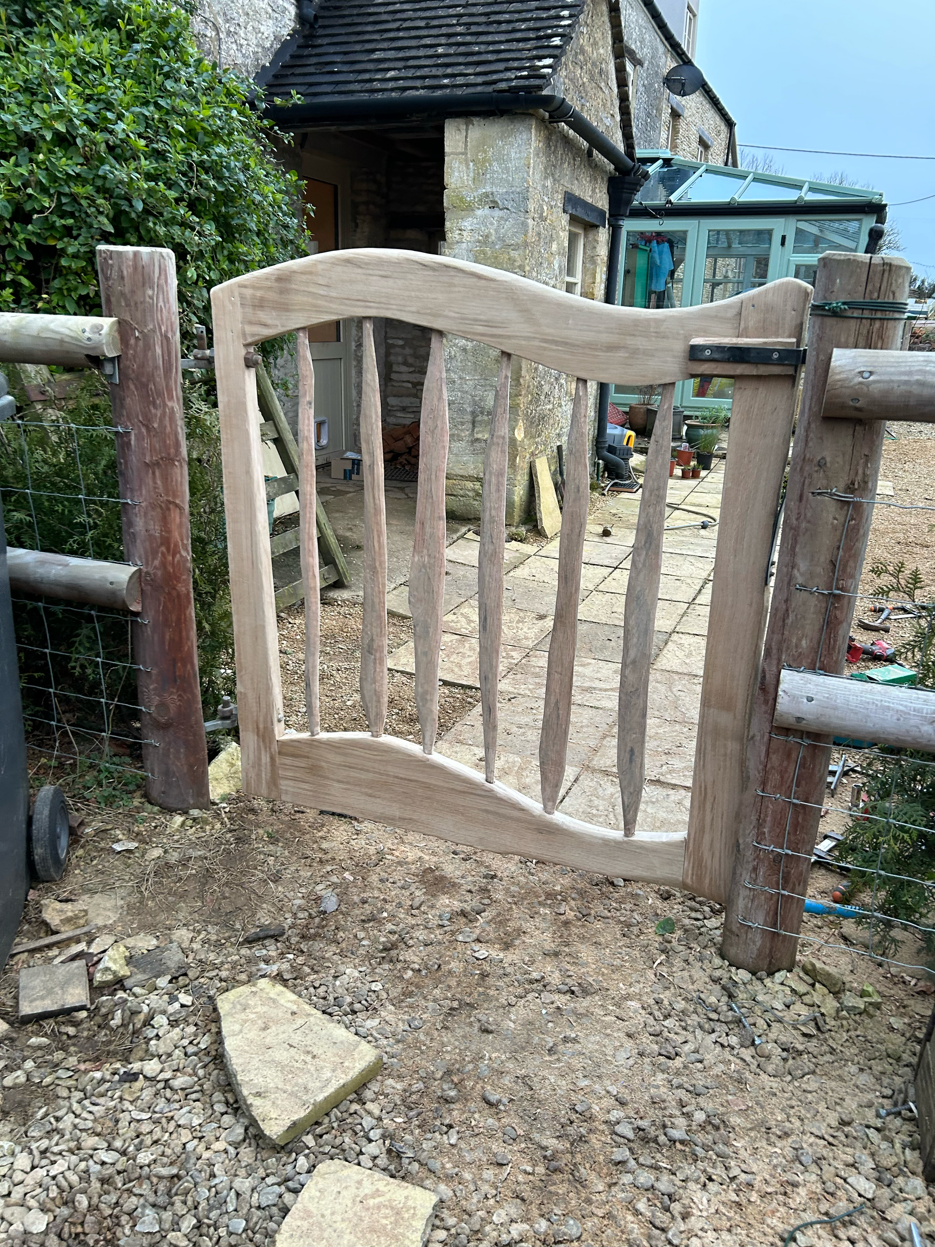 Unfinished small wooden gate attached to fence posts in a backyard.