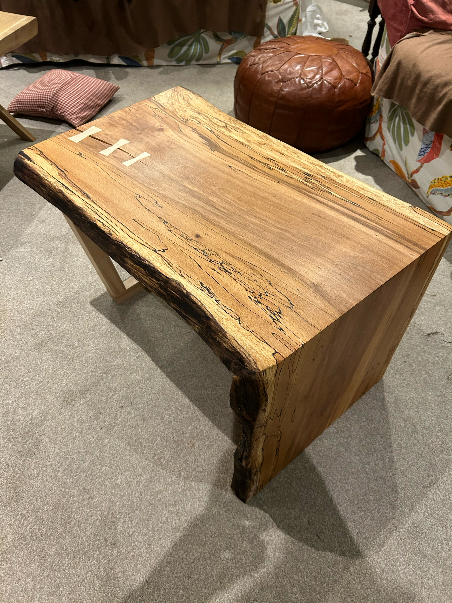 A rustic wooden table with a natural edge, placed on a carpeted floor in a cozy room.
