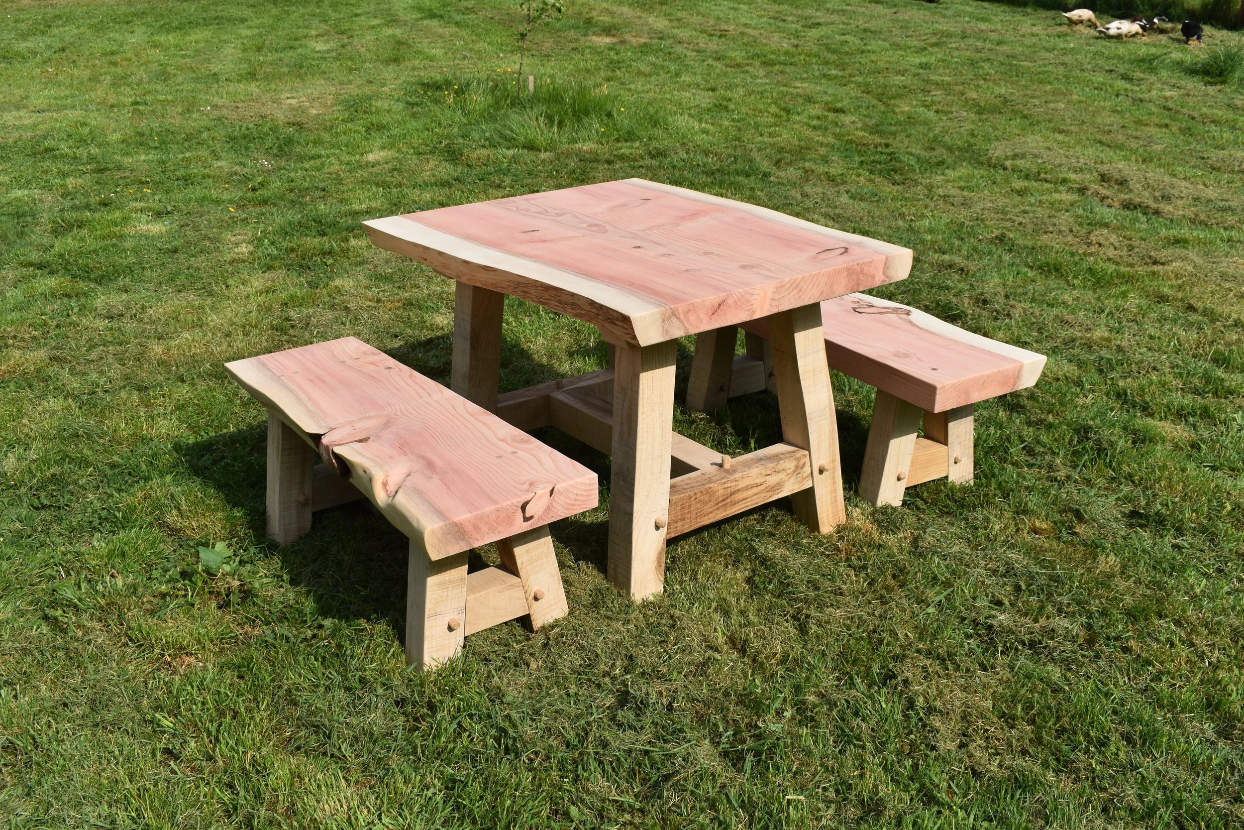 A wooden picnic table with two benches on a grassy field.
