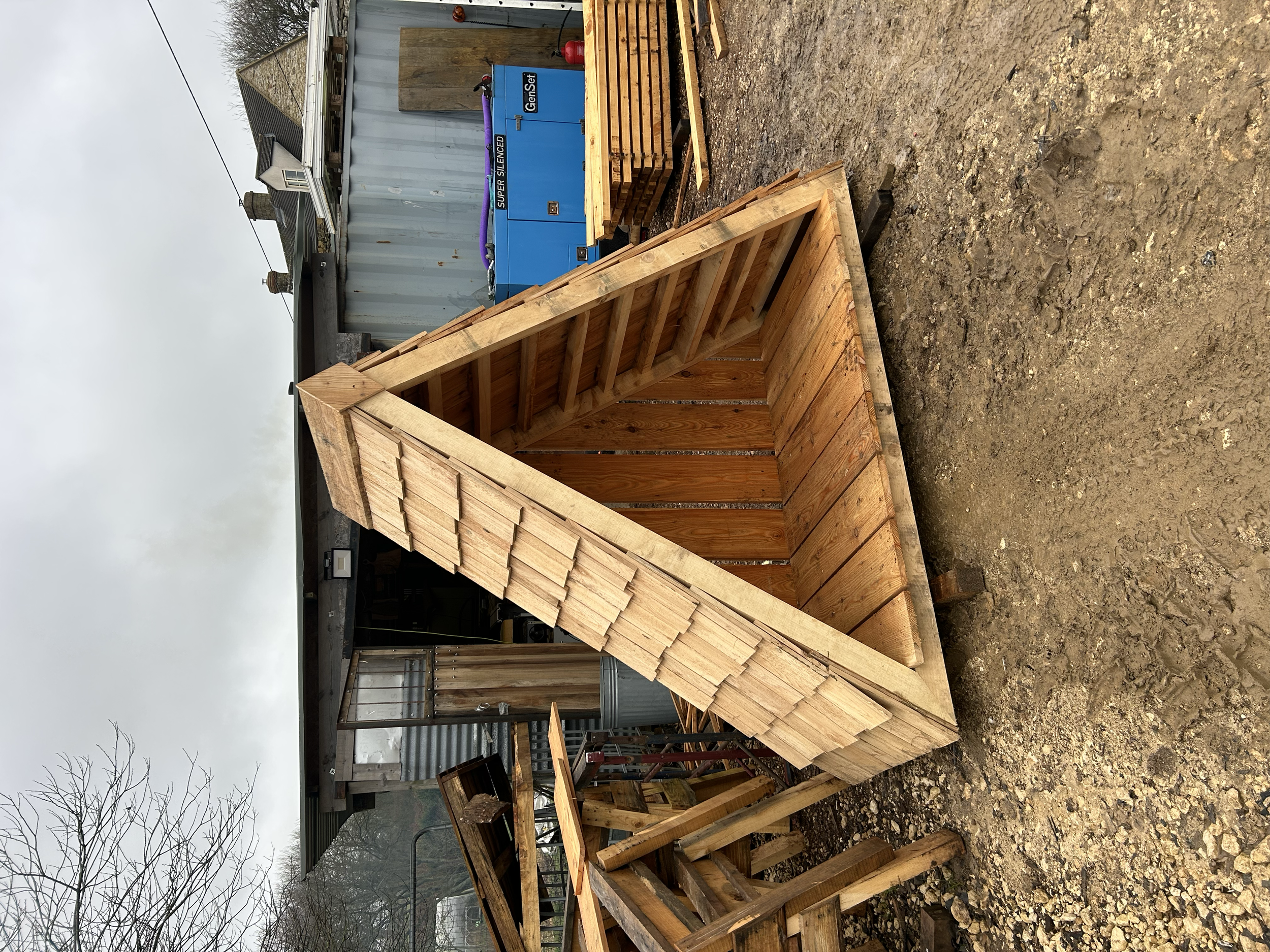 Wooden shed under construction with a triangular roof structure in an outdoor yard.