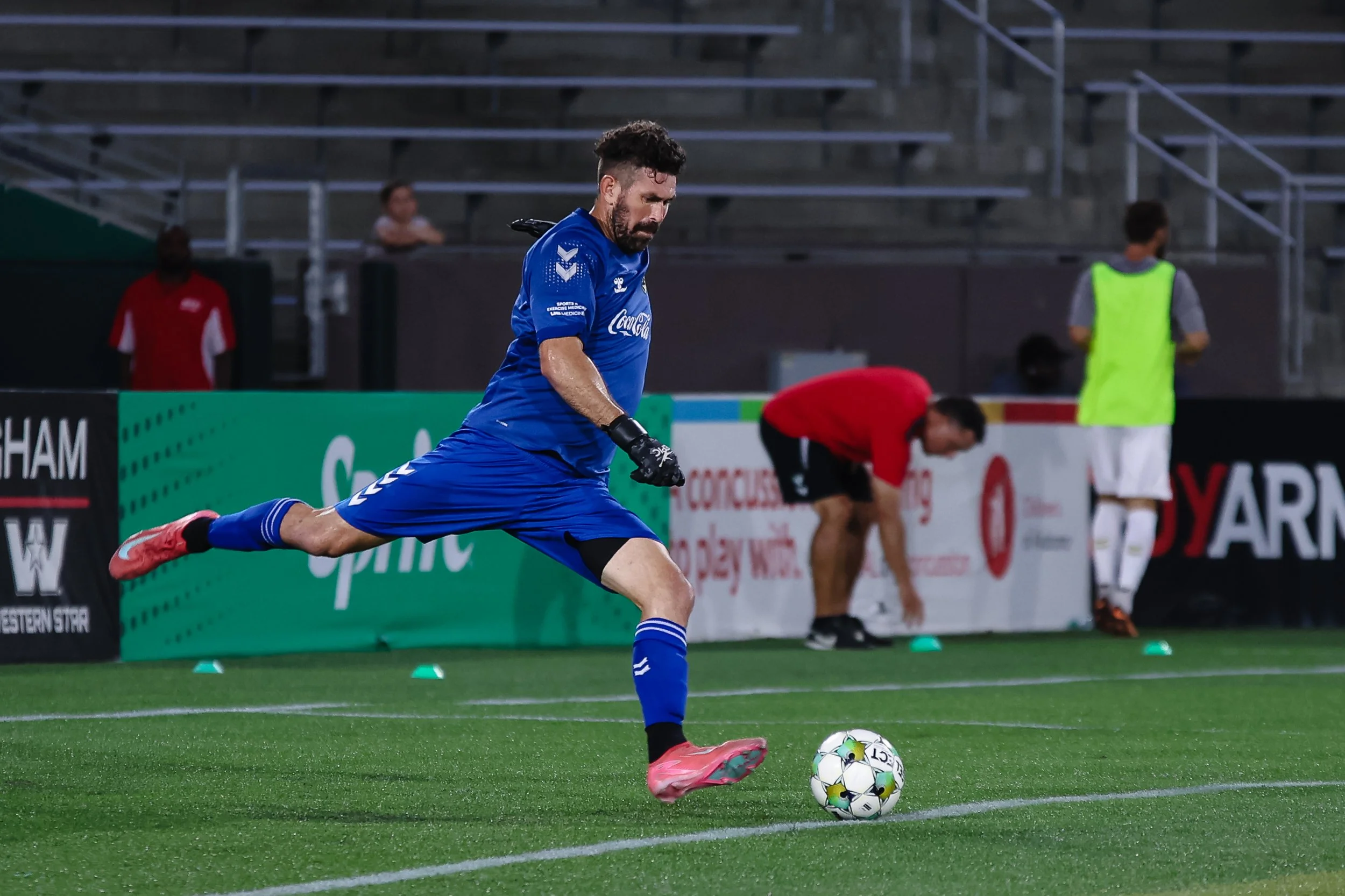 A soccer player in a blue uniform kicking a soccer ball on the field during a game or practice session.