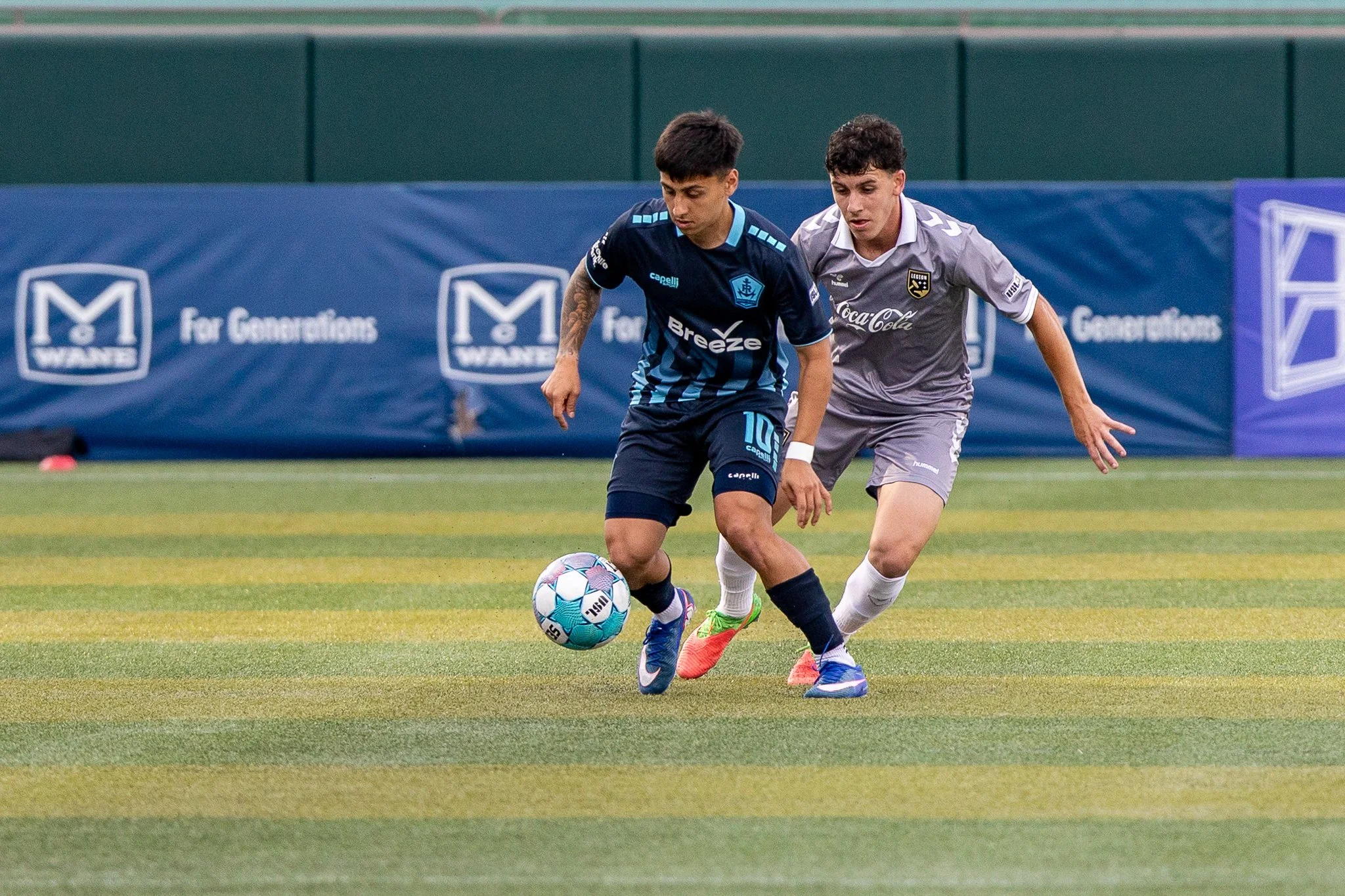Two young male soccer players competing for possession of a soccer ball on a green field during a match.