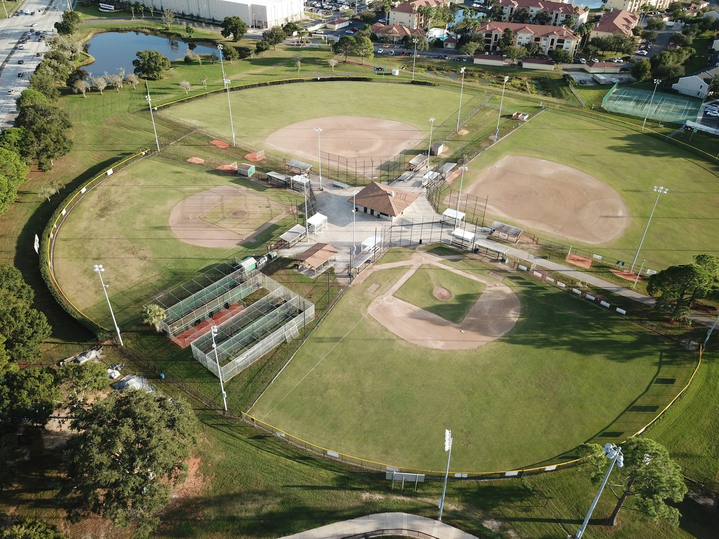 Aerial view of a baseball complex with multiple fields, fencing, and surrounding amenities in a park-like setting.