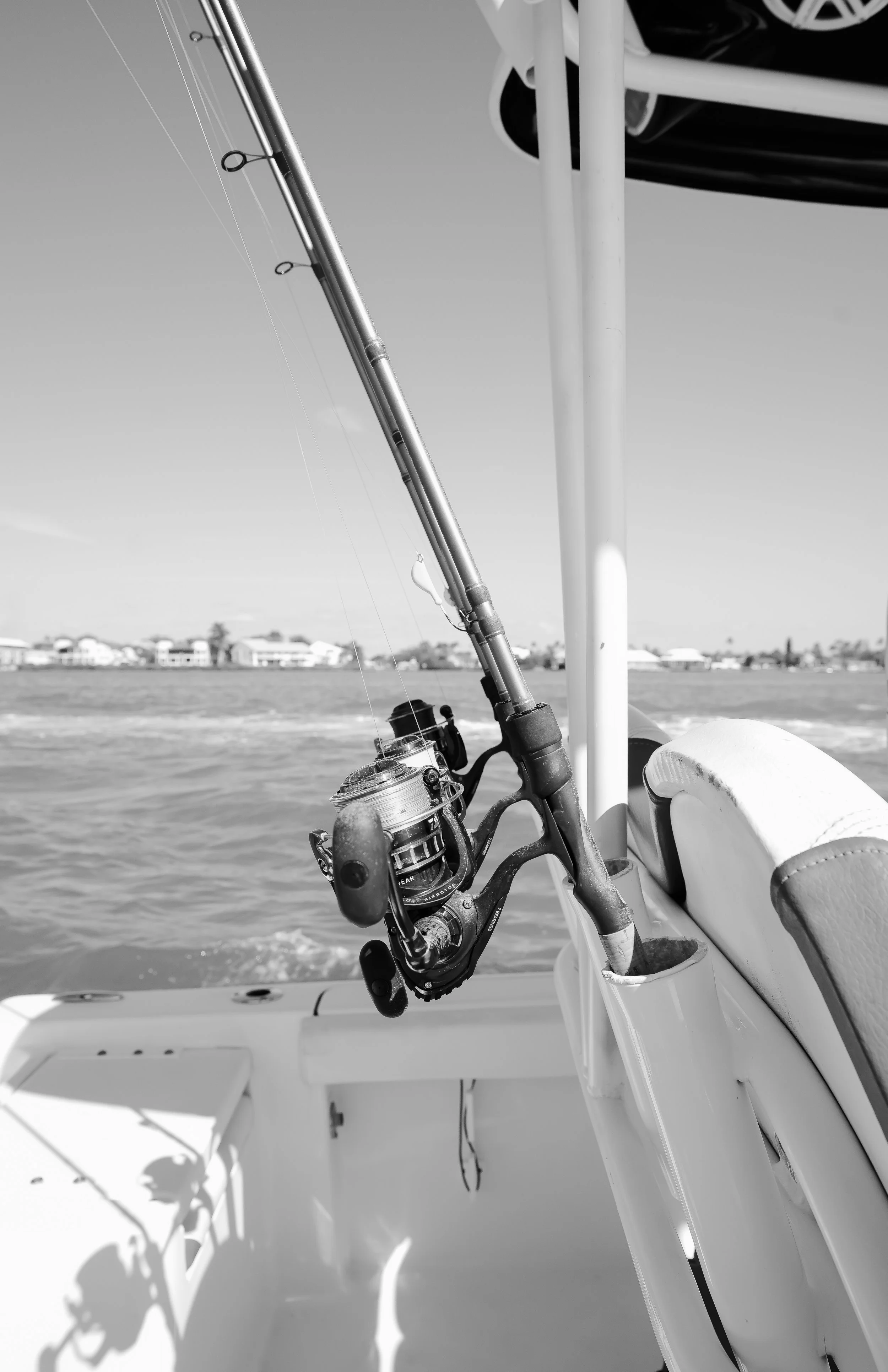A fishing rod mounted on a boat with water and shoreline in the background.