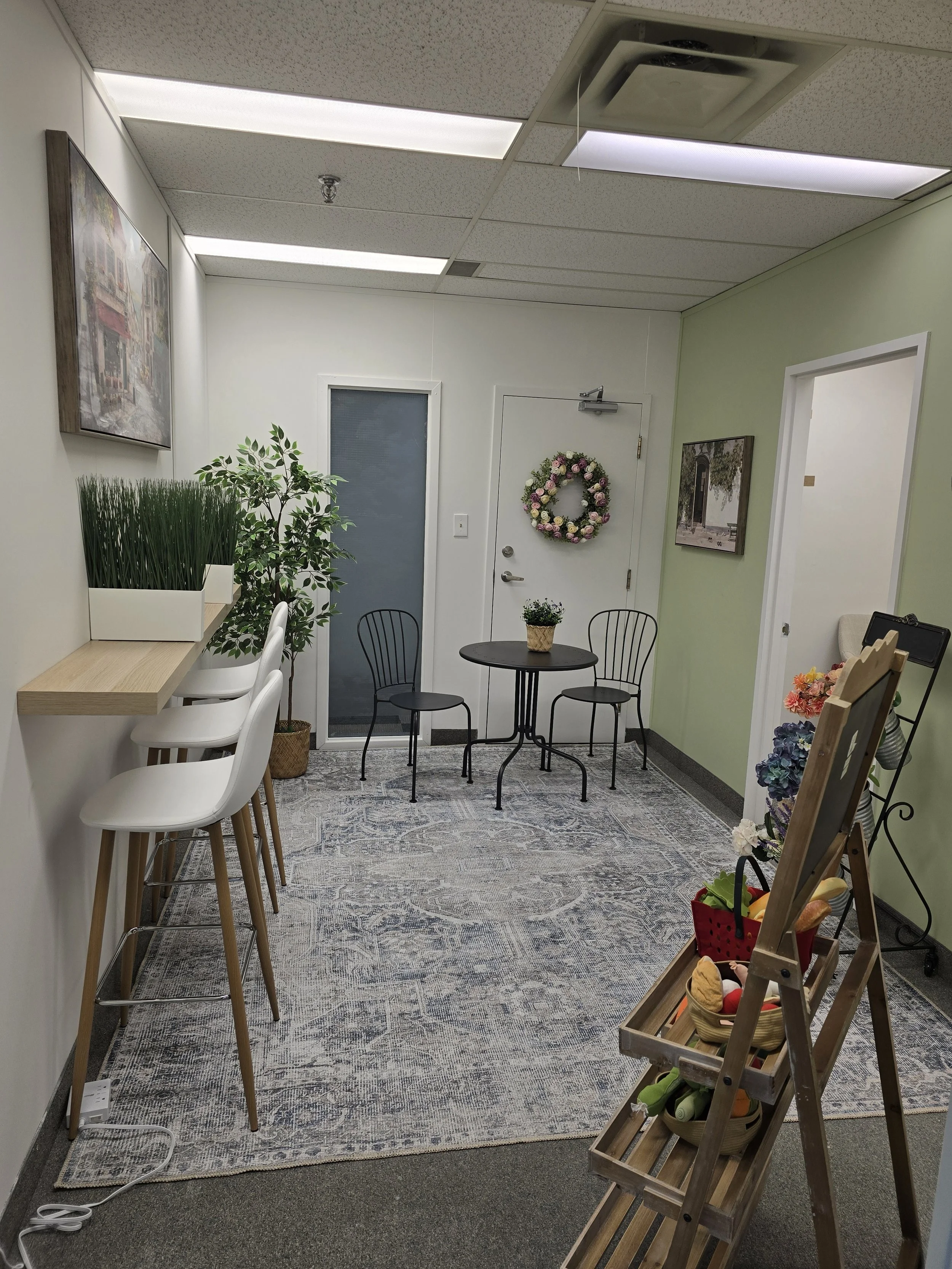 New reception area in the office expansion at Embark Psychology Calgary with seating for parents to work, bistro-style seating, and flowers and toy food stands for decor.
