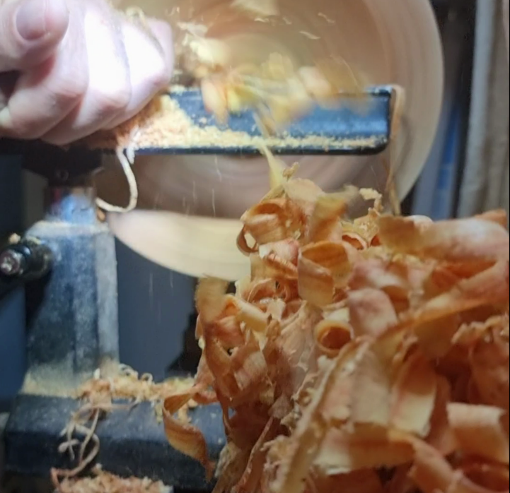 Woodturning on a lathe with wood shavings.