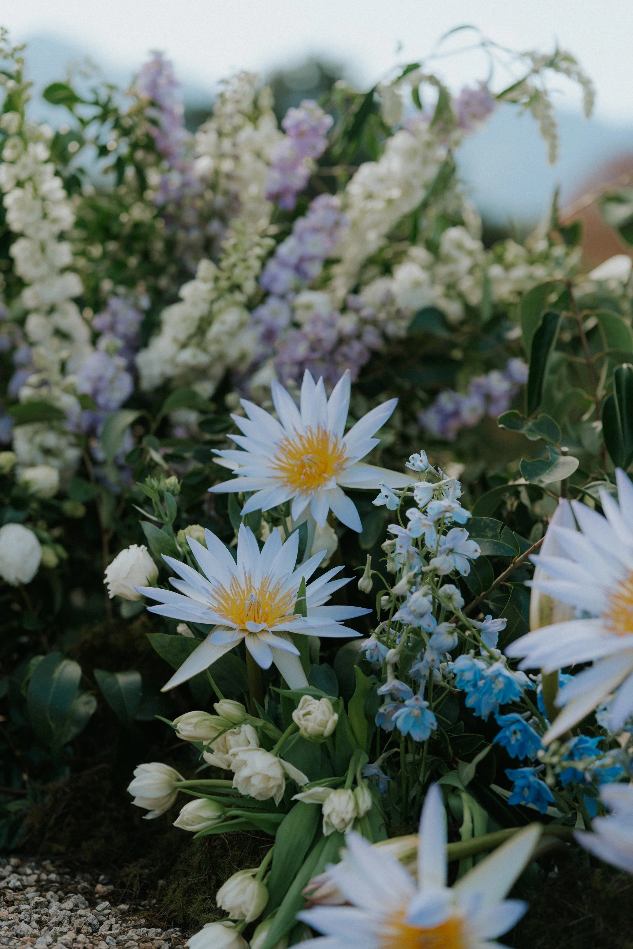 Close-up of a flower arrangement with white and purple flowers, including lilies, in a garden setting.